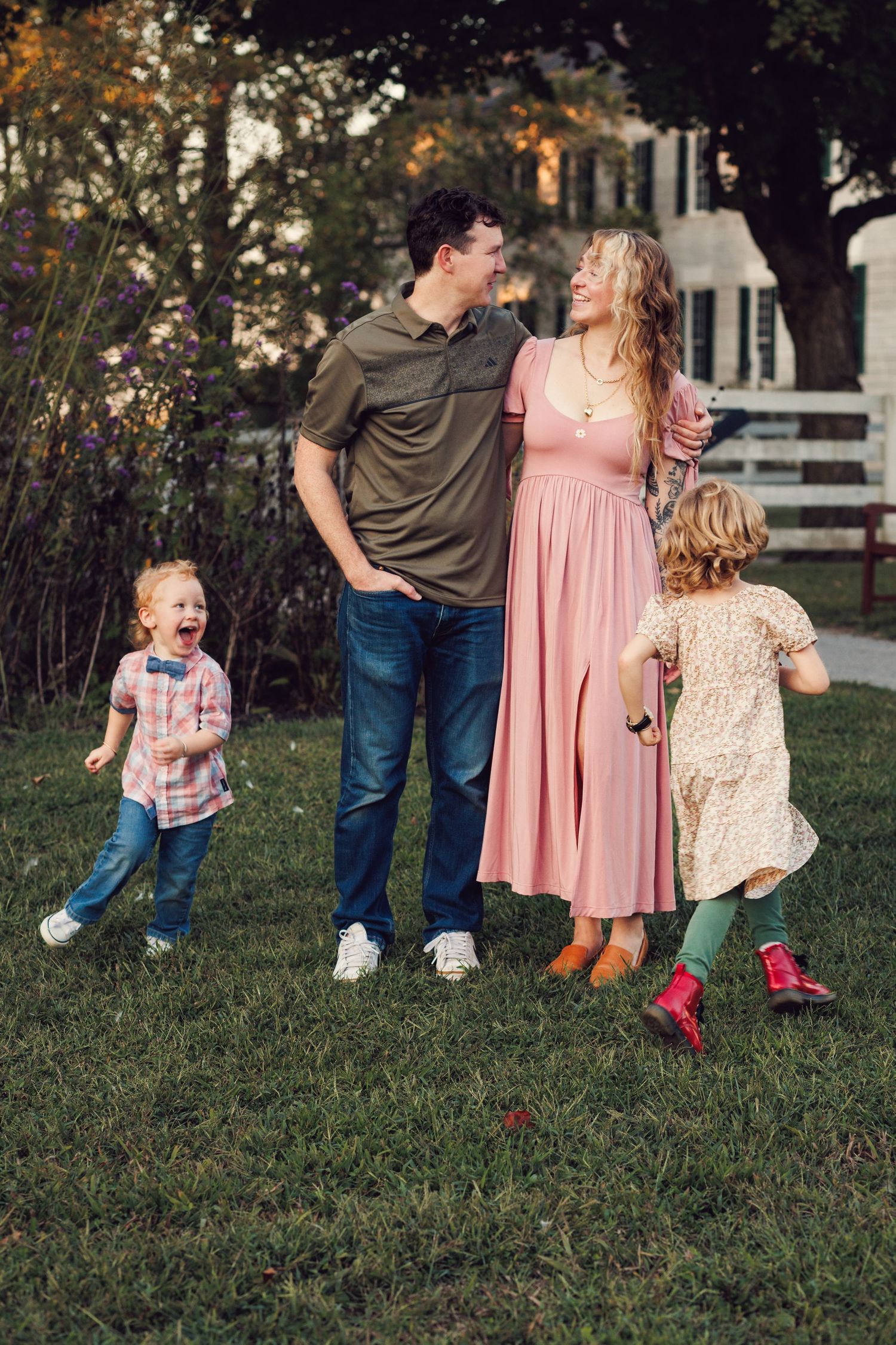 A family in casual attire walks and plays together on green grass during an outdoor photo session.
