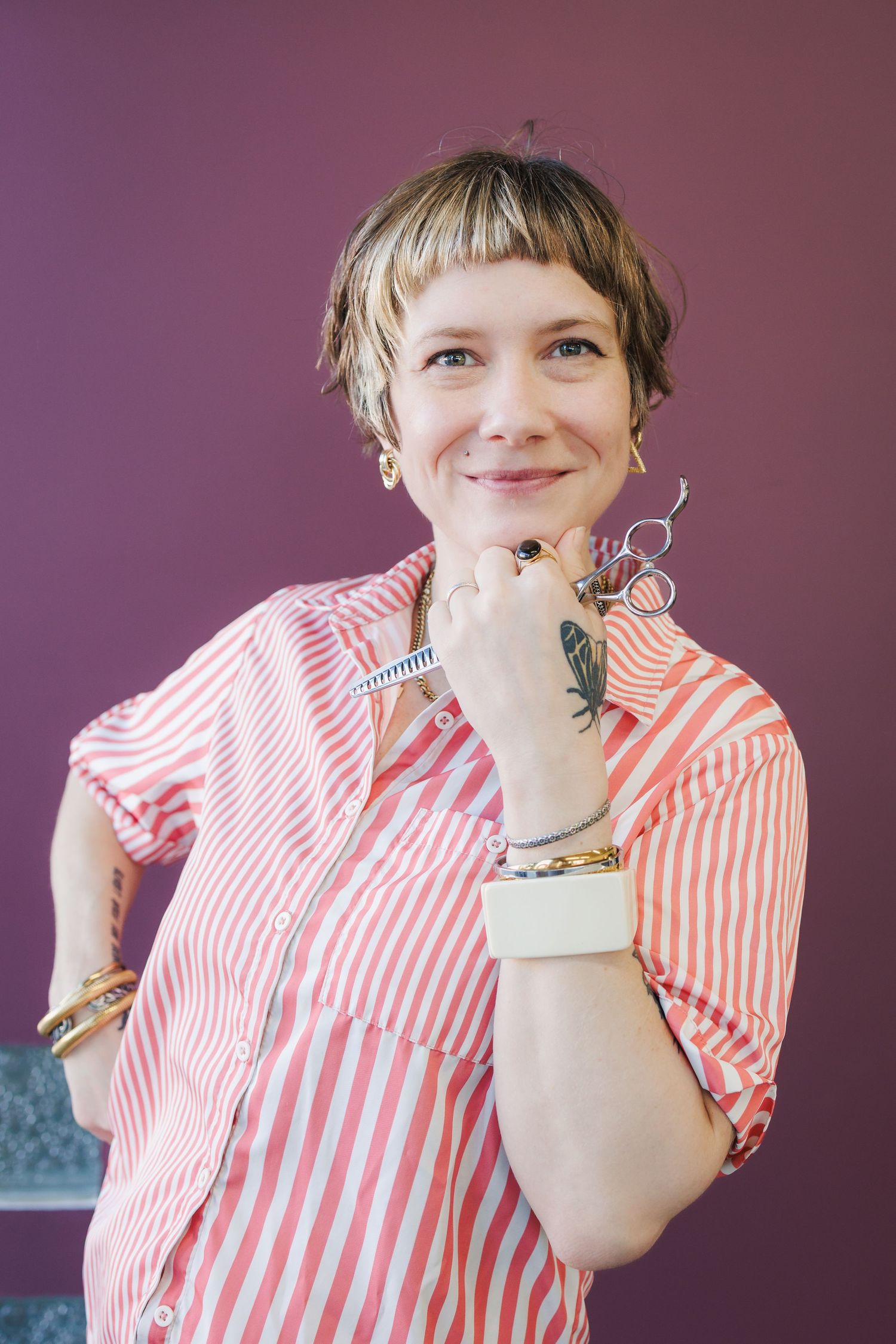 Person in pink and white striped shirt smiles while holding keys against purple wall background.