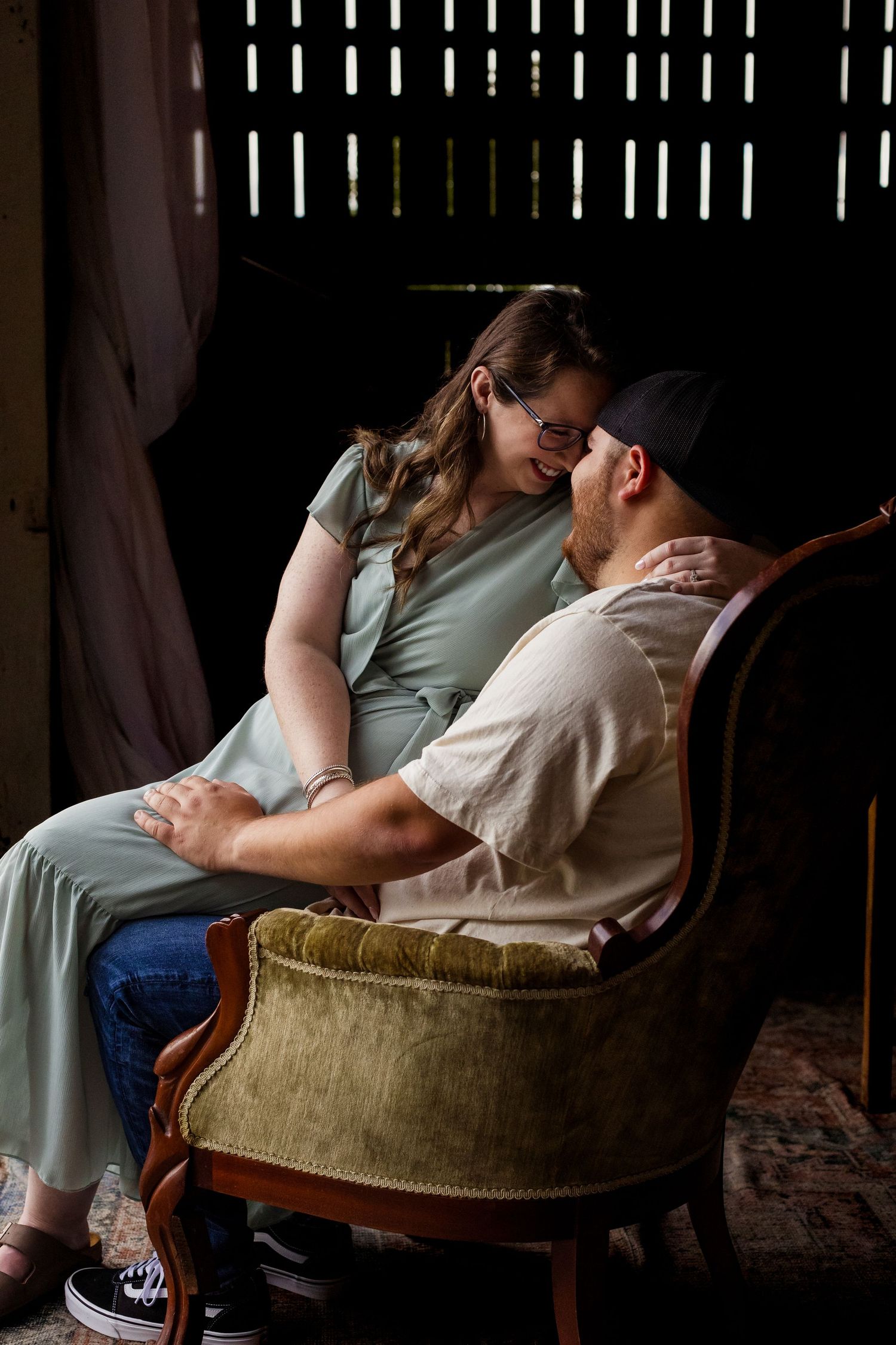 A romantic couple shares an intimate moment while sitting in a vintage velvet armchair.