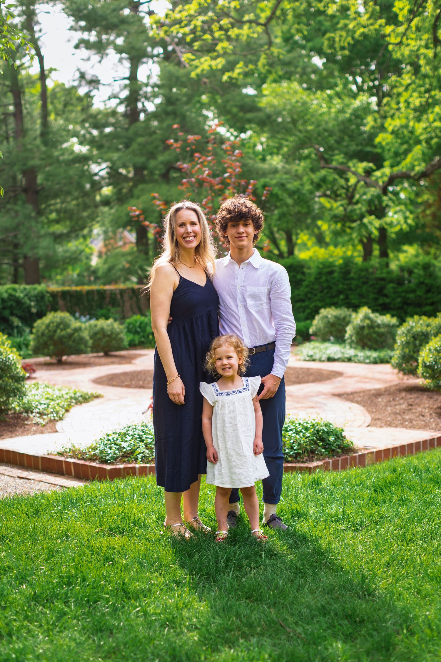 A family enjoys a casual summer photoshoot together in a lush garden setting with brick landscaping.