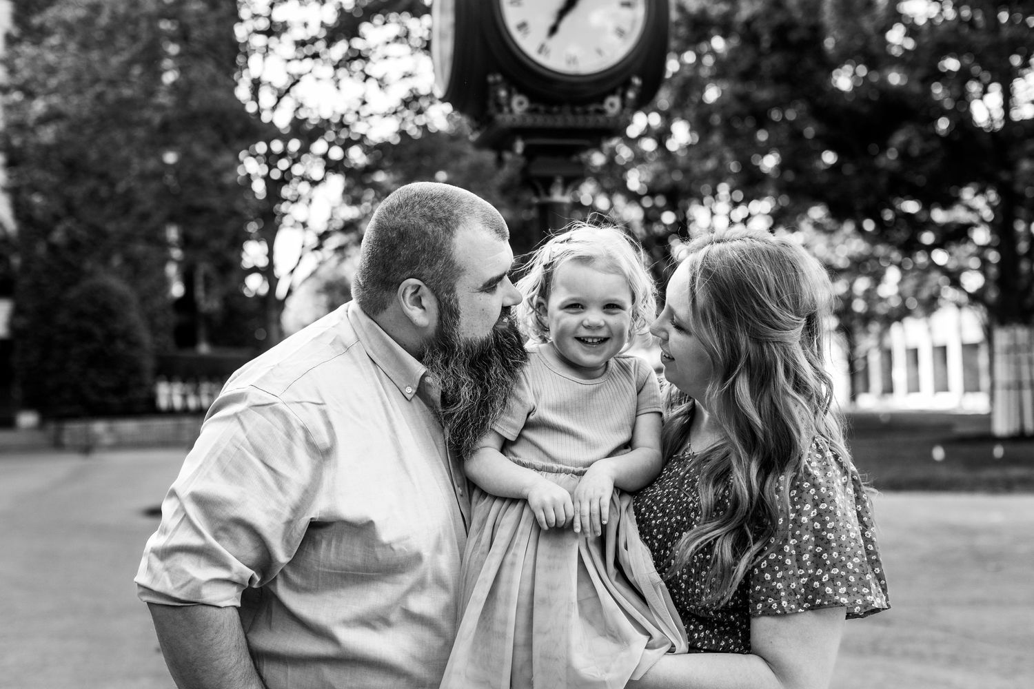 A series of black and white candid outdoor family portraits showing joyful moments and interactions in a park setting.