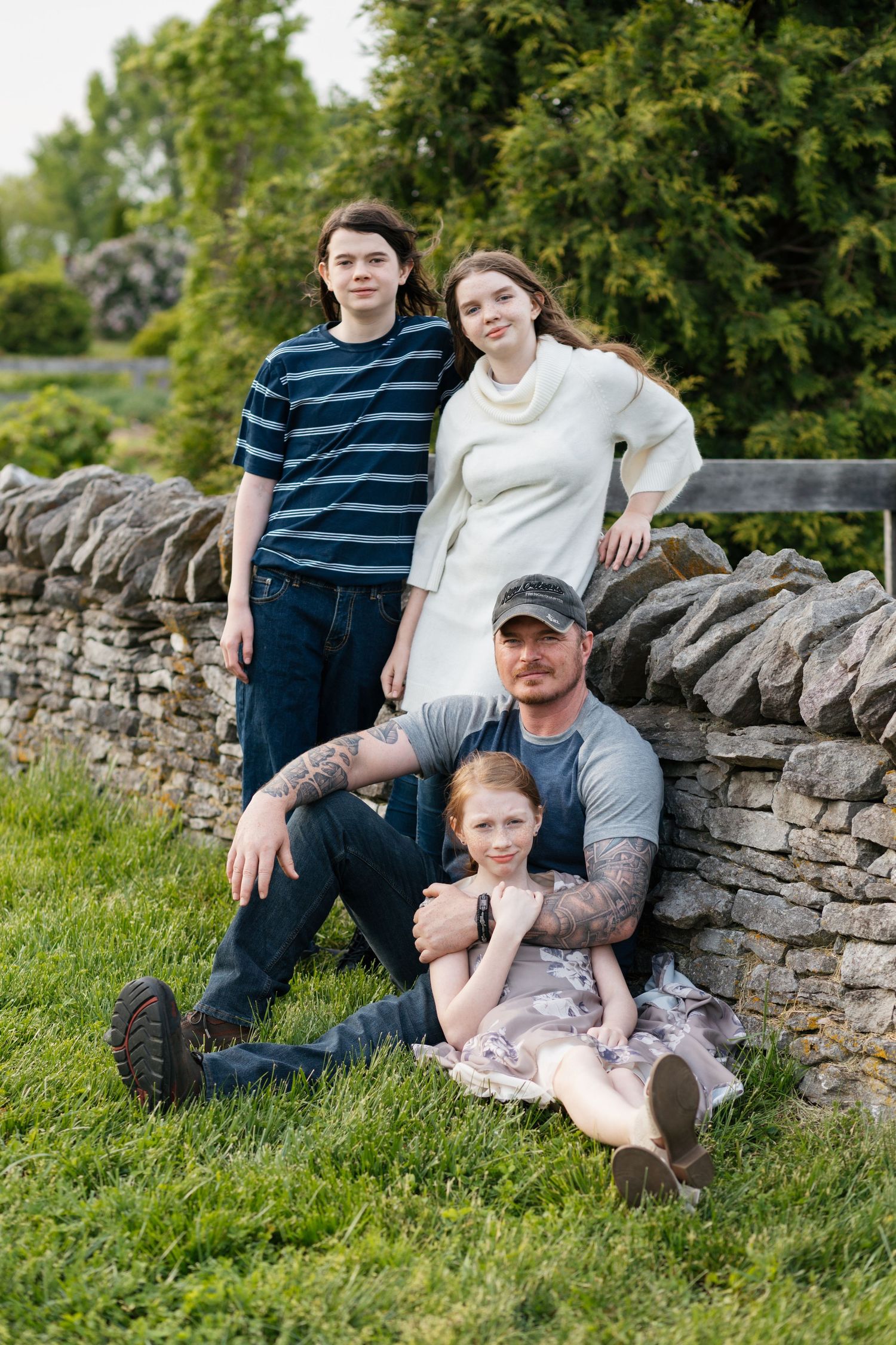 A casual family portrait against a rustic stone wall in a garden setting.