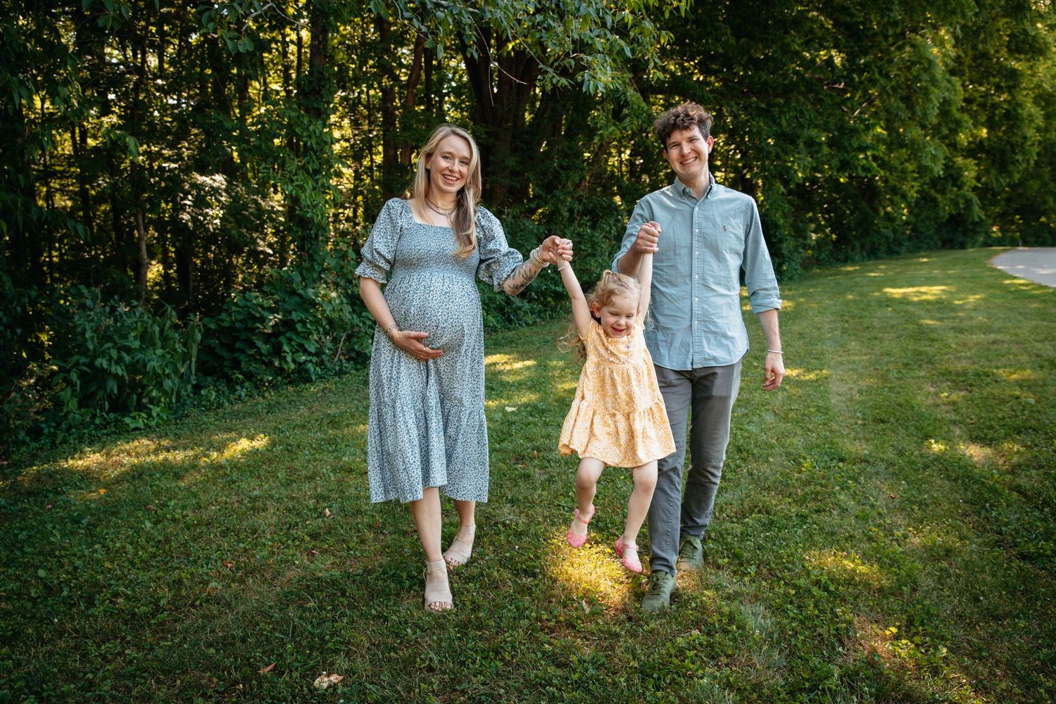 A family in a sunlit garden holding hands while walking together on a summer afternoon.