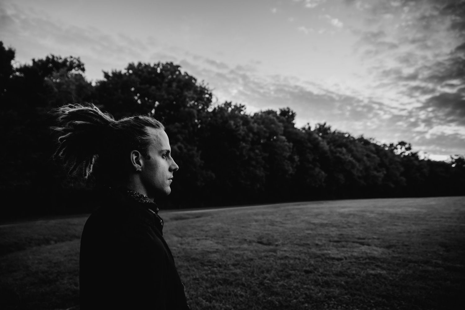 Silhouette profile against dramatic sunset sky with trees in background.