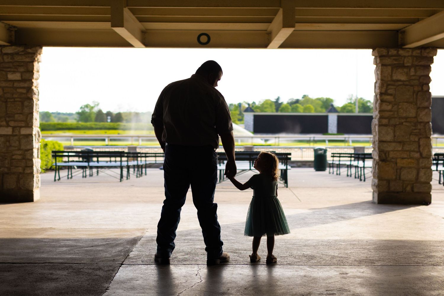 A sequence of silhouettes show someone helping a small child learn to walk in an outdoor covered area.