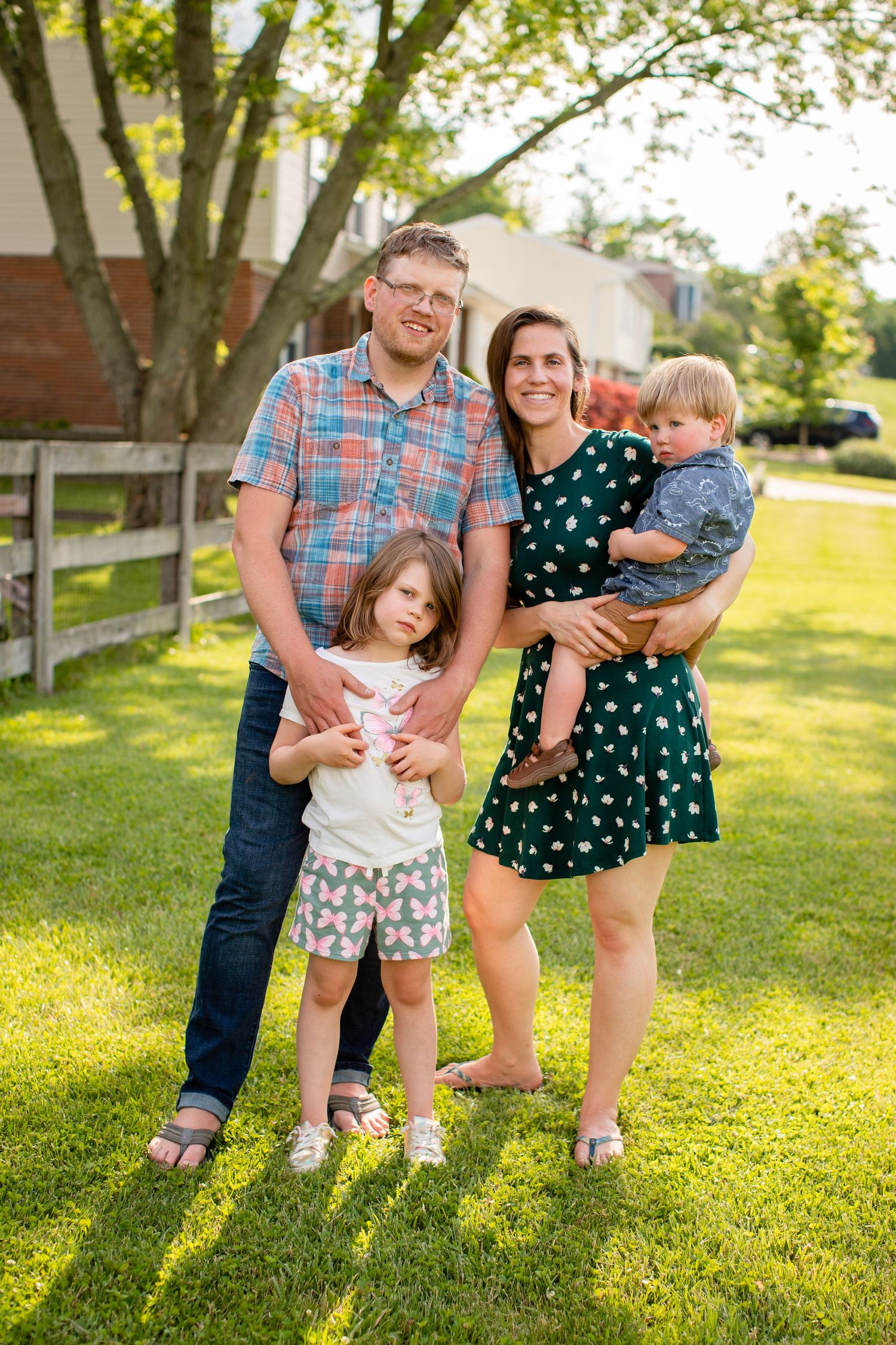 Family posing together on a sunny lawn with trees and buildings in the background.