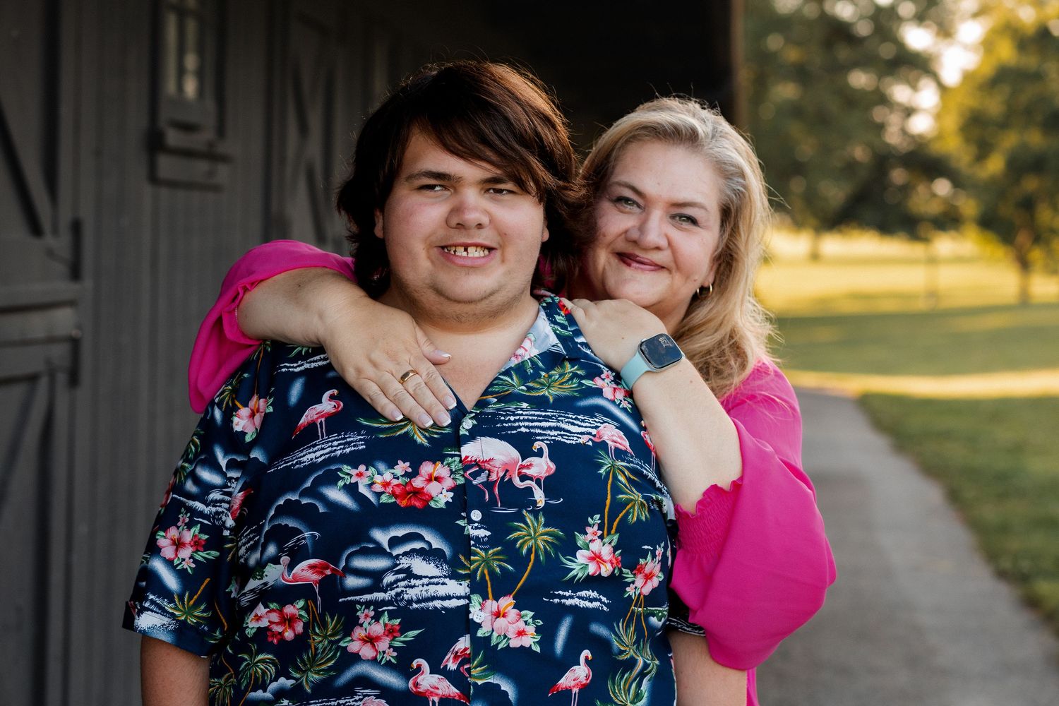 People wearing floral and pink clothing embrace and laugh together during an outdoor photo session at sunset.