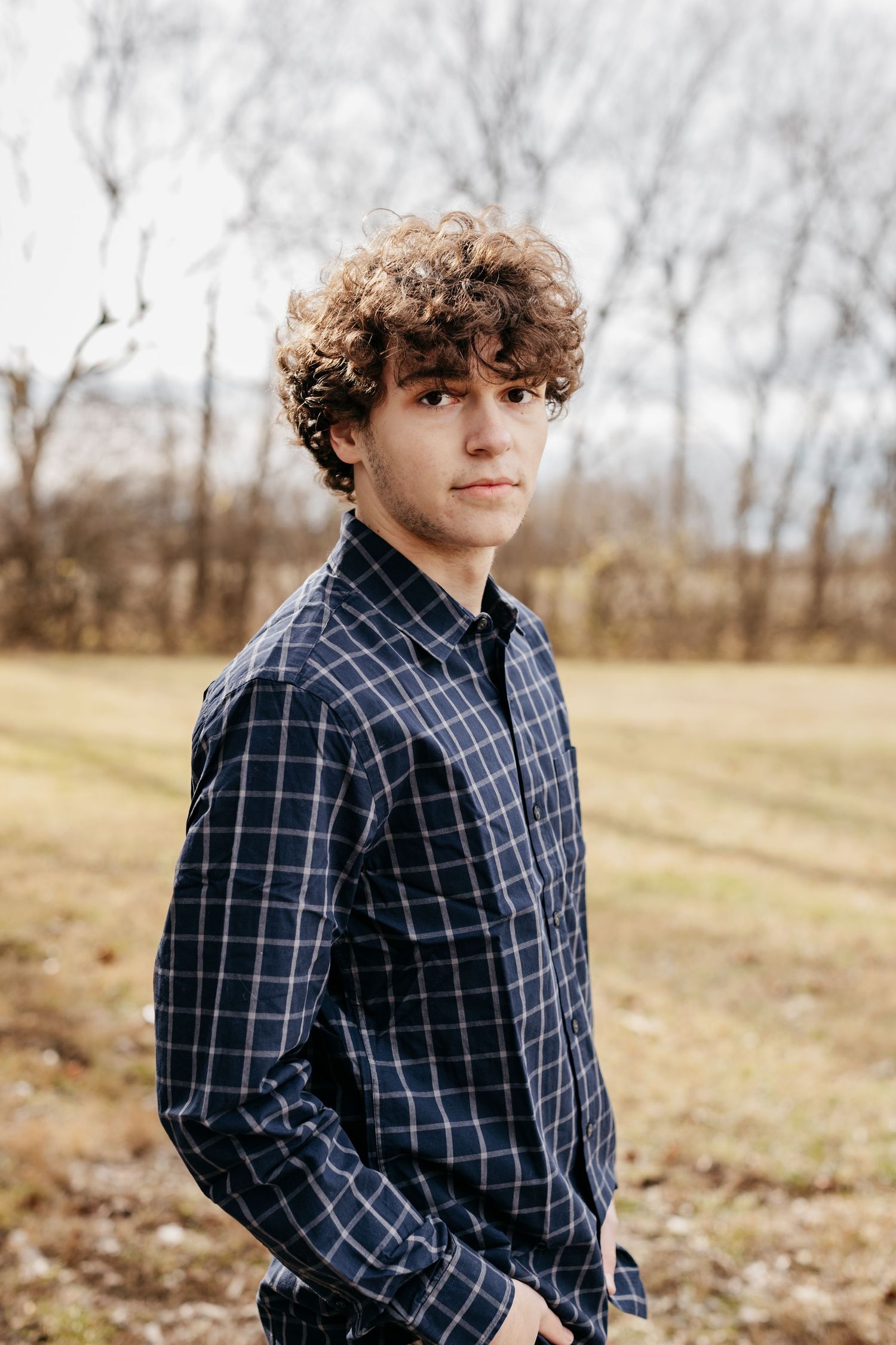 Outdoor portrait of someone wearing navy plaid shirt against autumn landscape.