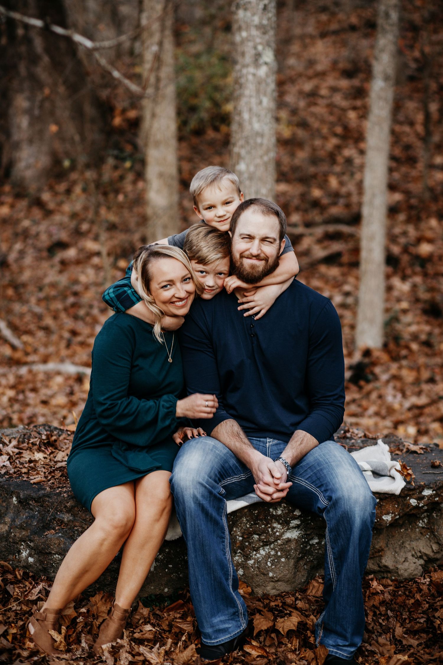A family group sits together on a rock in an autumn forest setting.