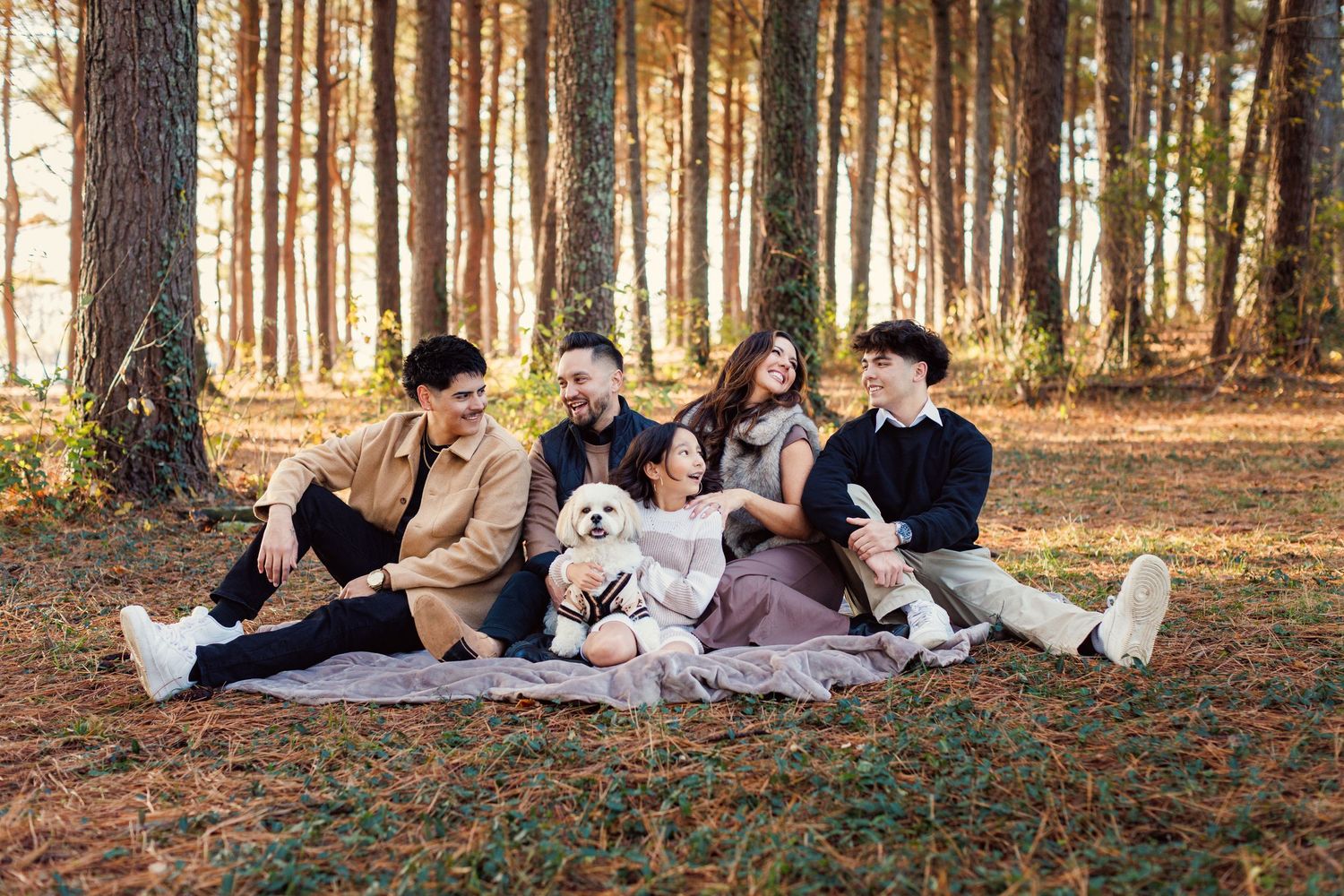 A group of people lying on autumn leaves in a forest during a casual outdoor photoshoot.