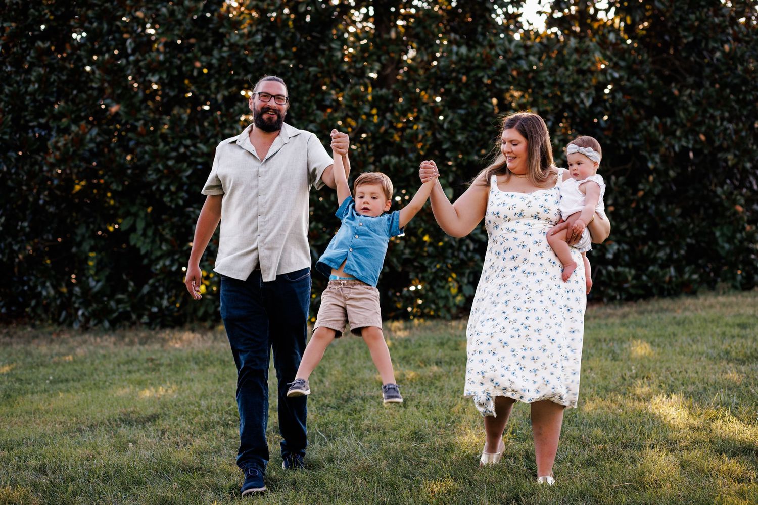 A family playfully runs and spins together in a backyard during golden hour with trees in the background.