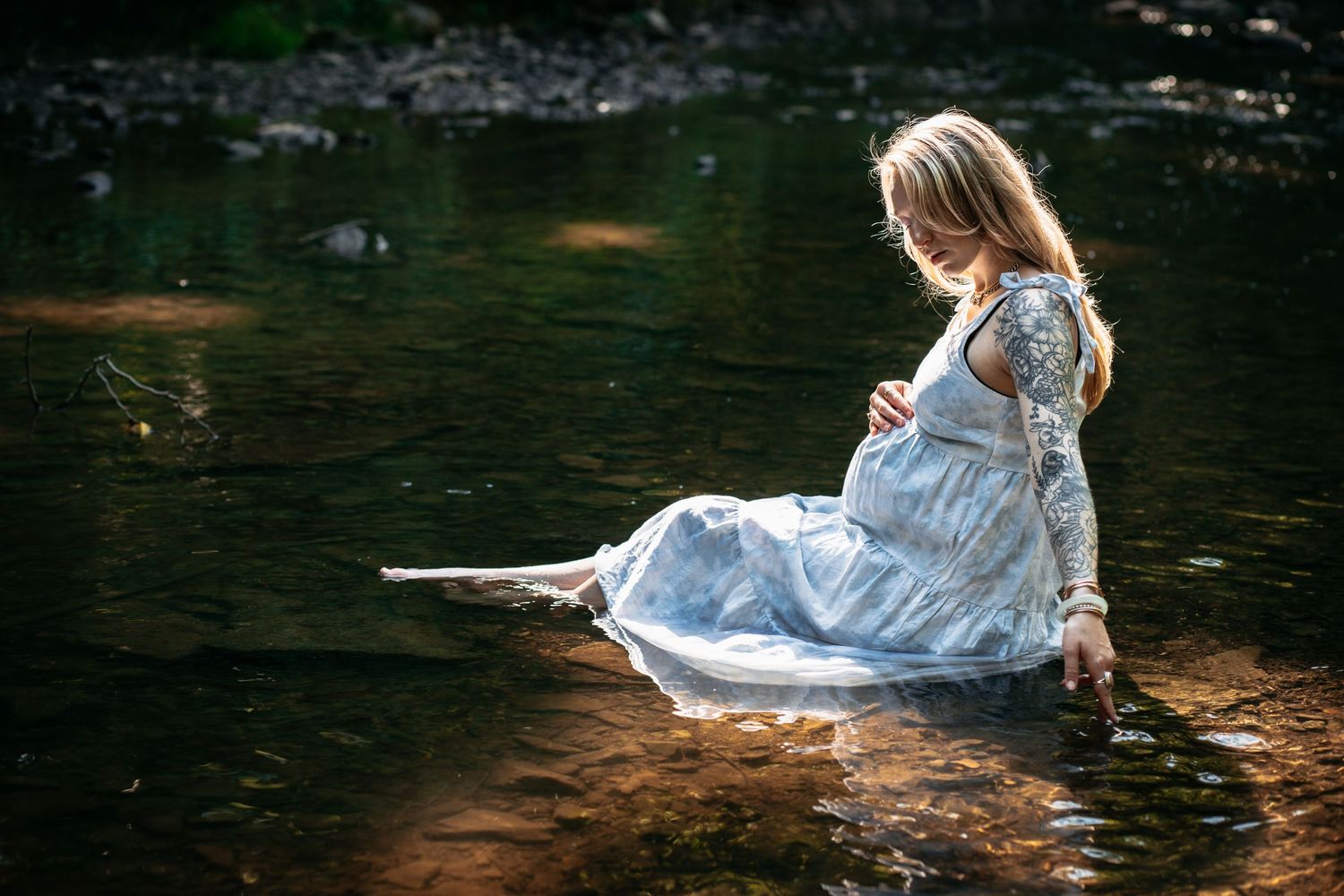 A dreamy portrait of a mother-to-be in white dress sitting by a stream.