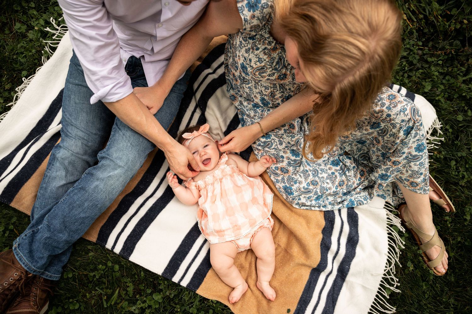 Family lying on striped blanket in grass playing with baby.