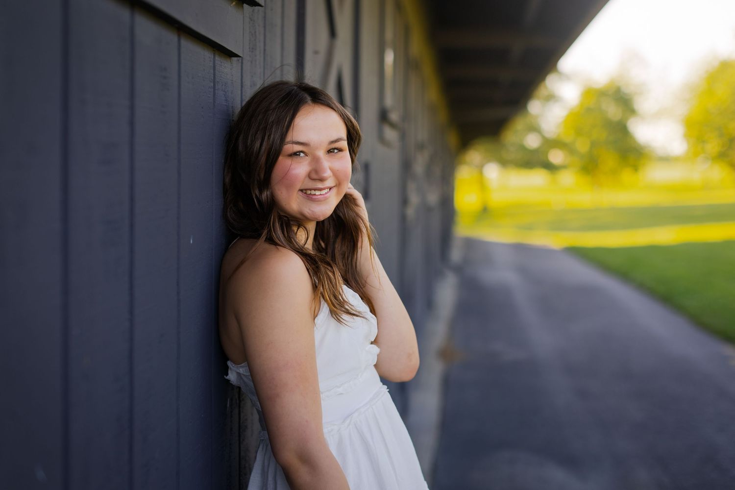 Young woman in a white dress poses for romantic outdoor portraits against navy blue garage doors and natural light.