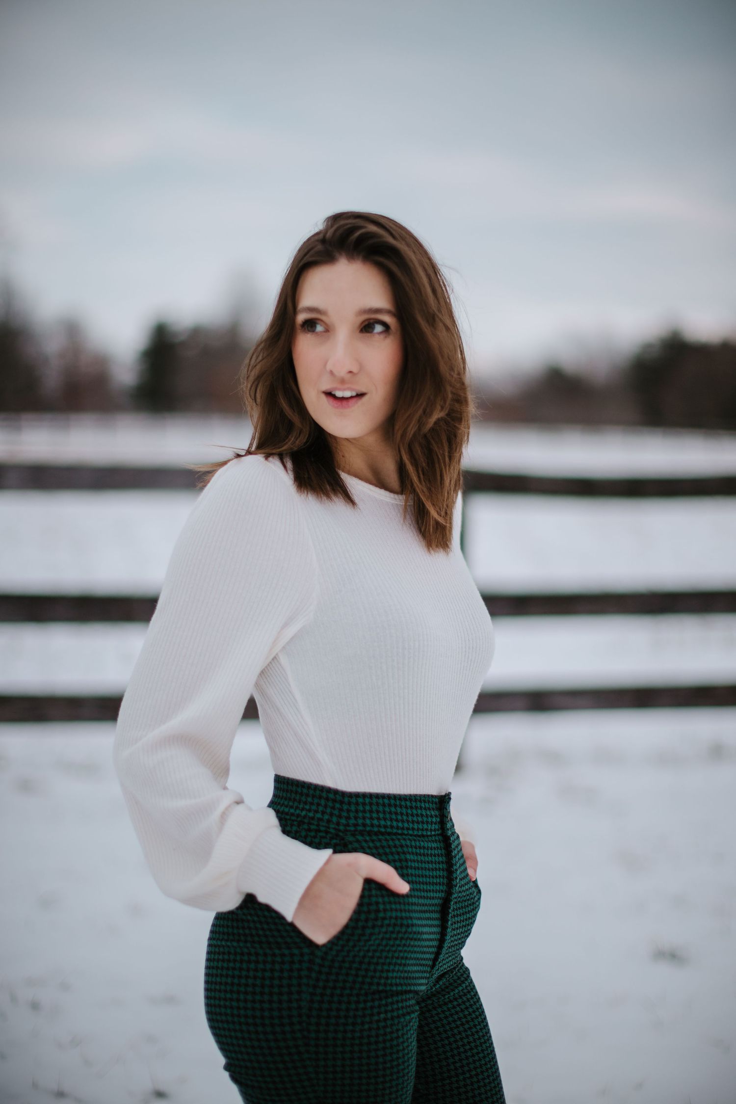 Winter fashion look with white sweater and green plaid pants against snowy backdrop.