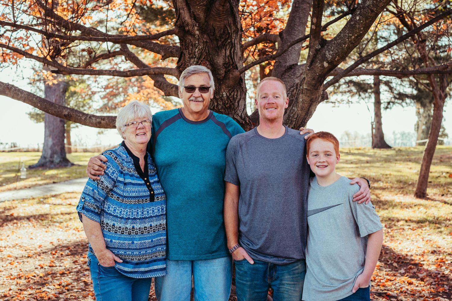 Four people stand together under an autumn tree with golden leaves during a family photo session.