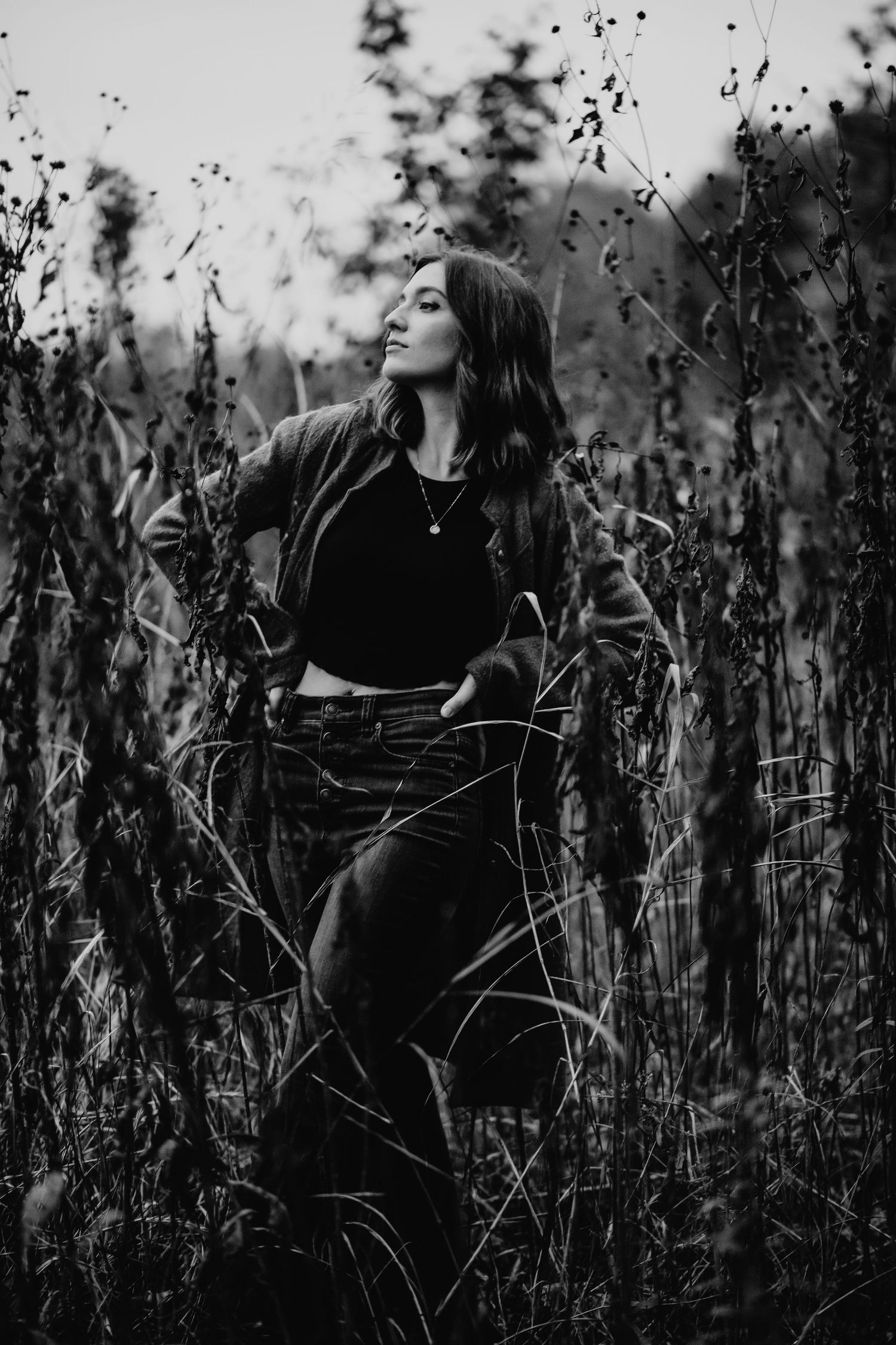Atmospheric black and white portrait of a woman standing among tall grasses in nature.