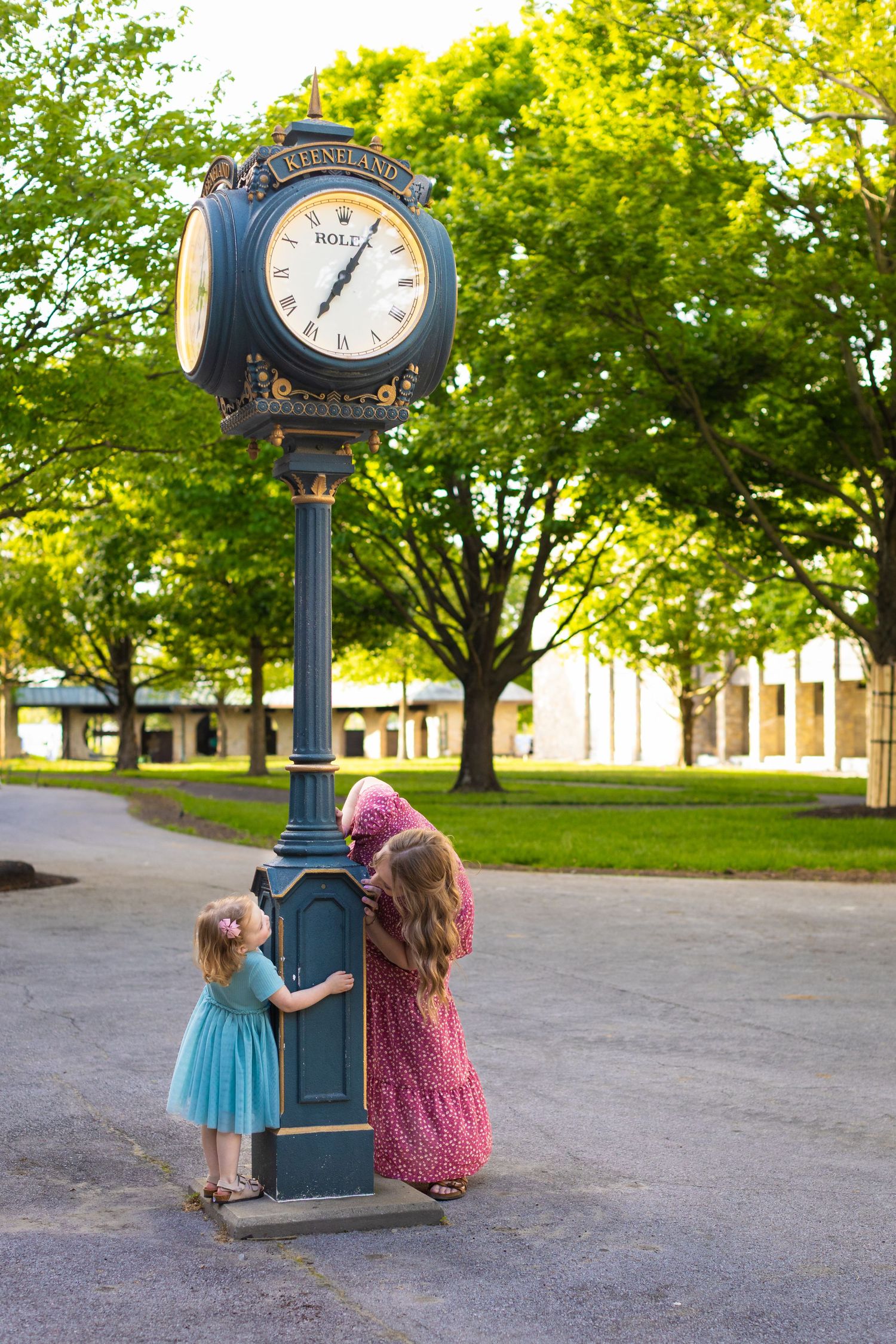 Vintage clock post stands in a green park setting as two figures look at its classic design in evening sunlight.