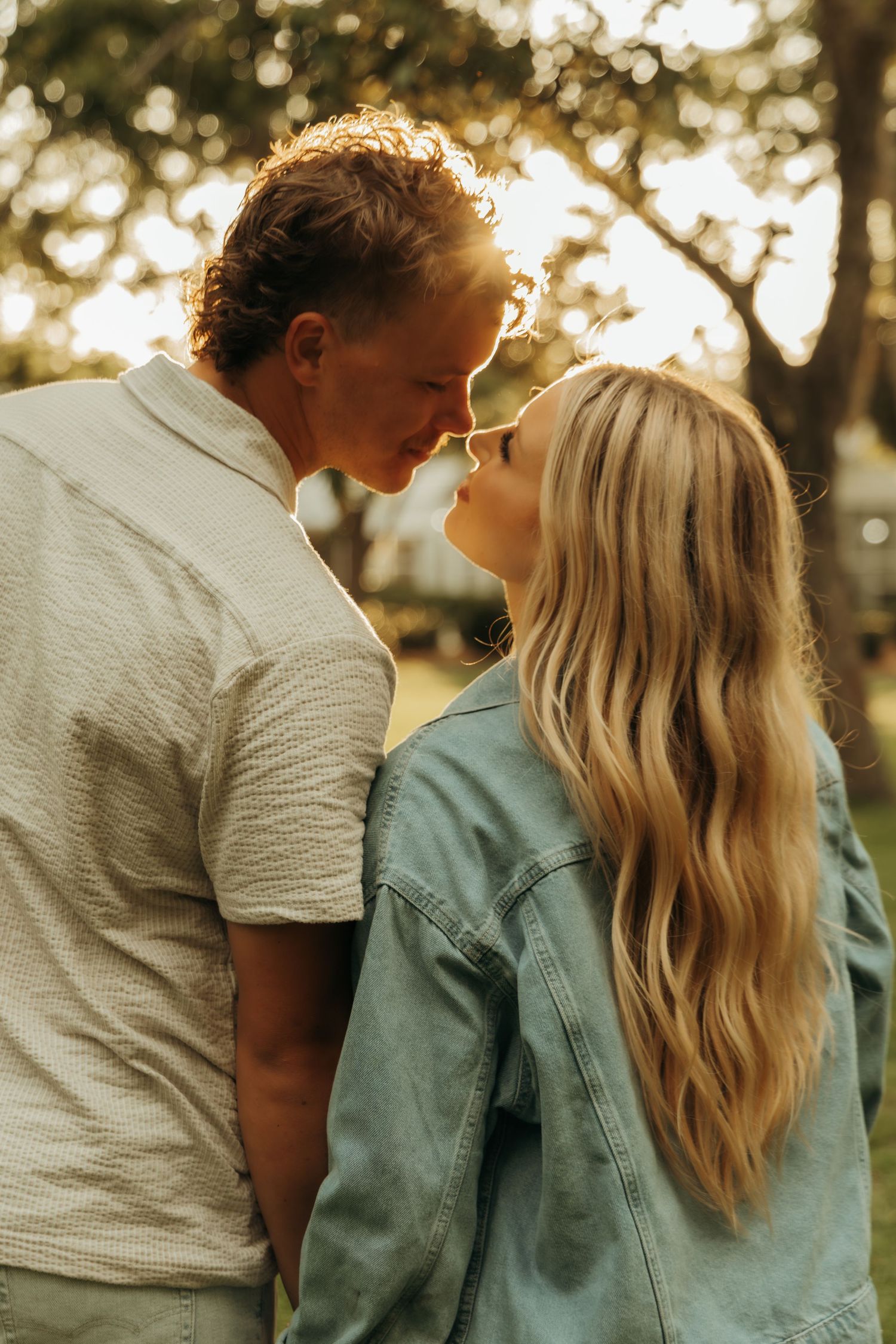 Romantic golden hour portrait of couple in casual attire against sunlit background.