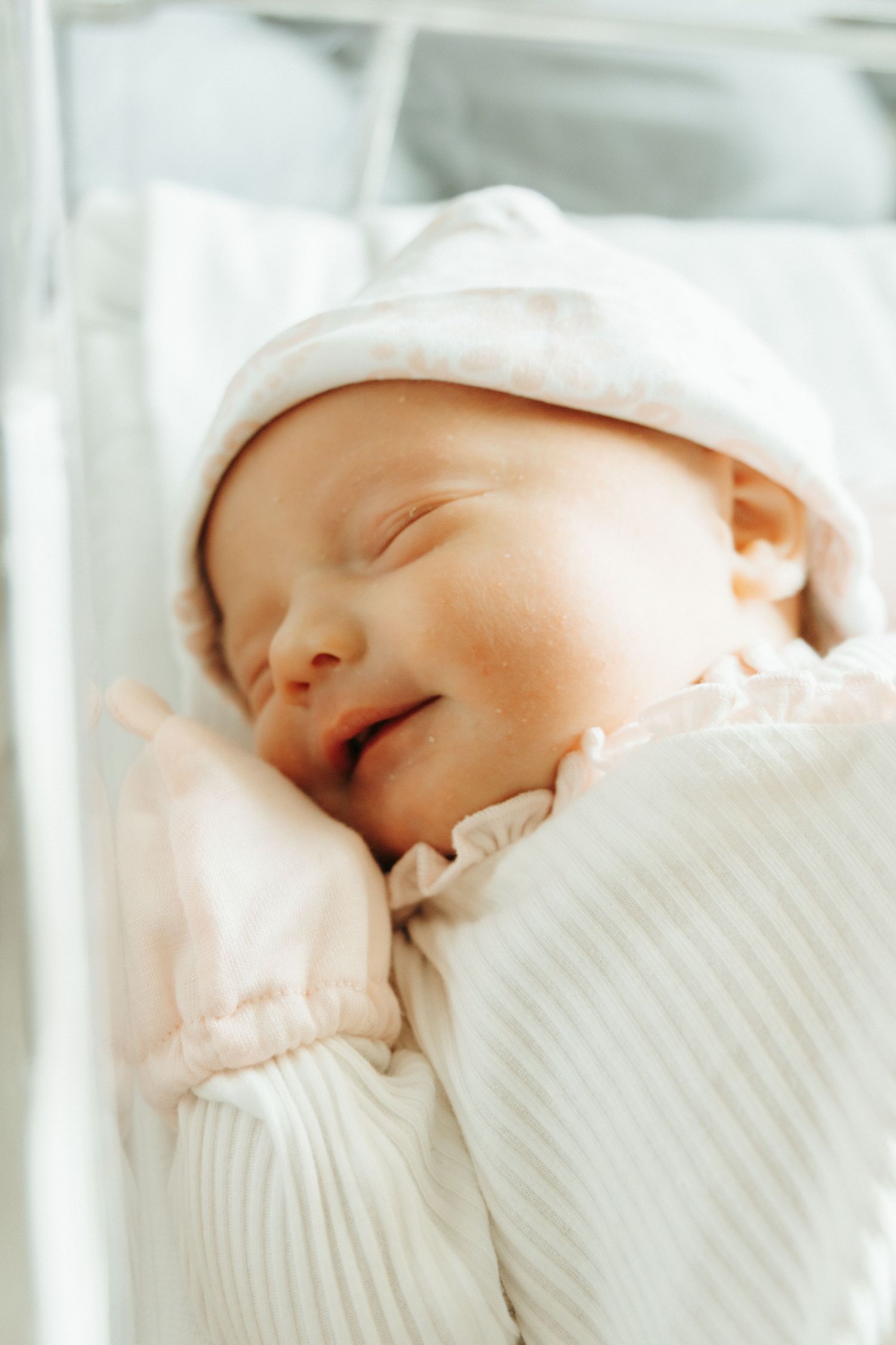 A sleeping newborn baby wearing a white knit sweater and hat smiles peacefully while resting.