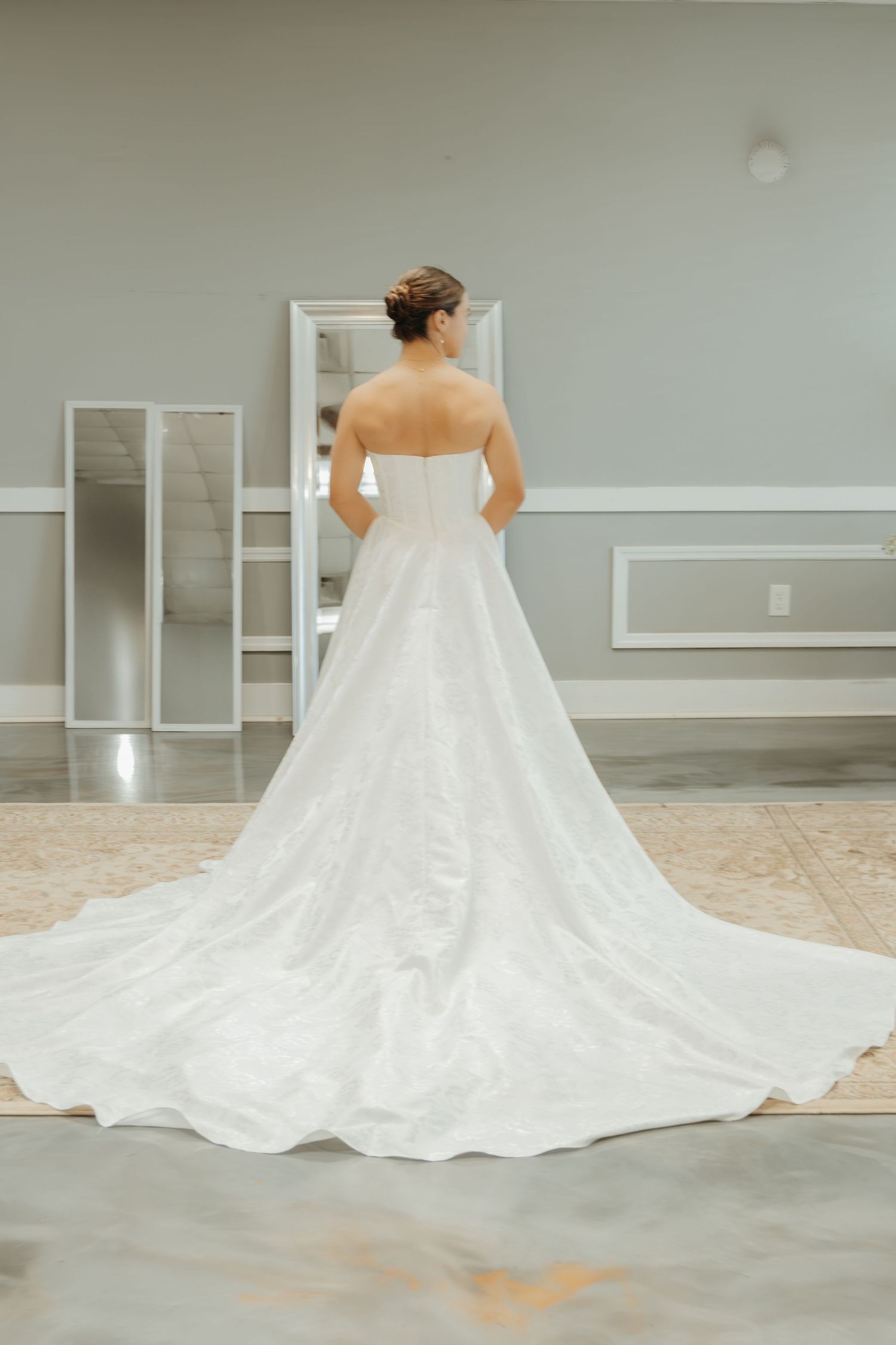 Back view of a bride wearing a strapless wedding gown with dramatic train in a gray room.