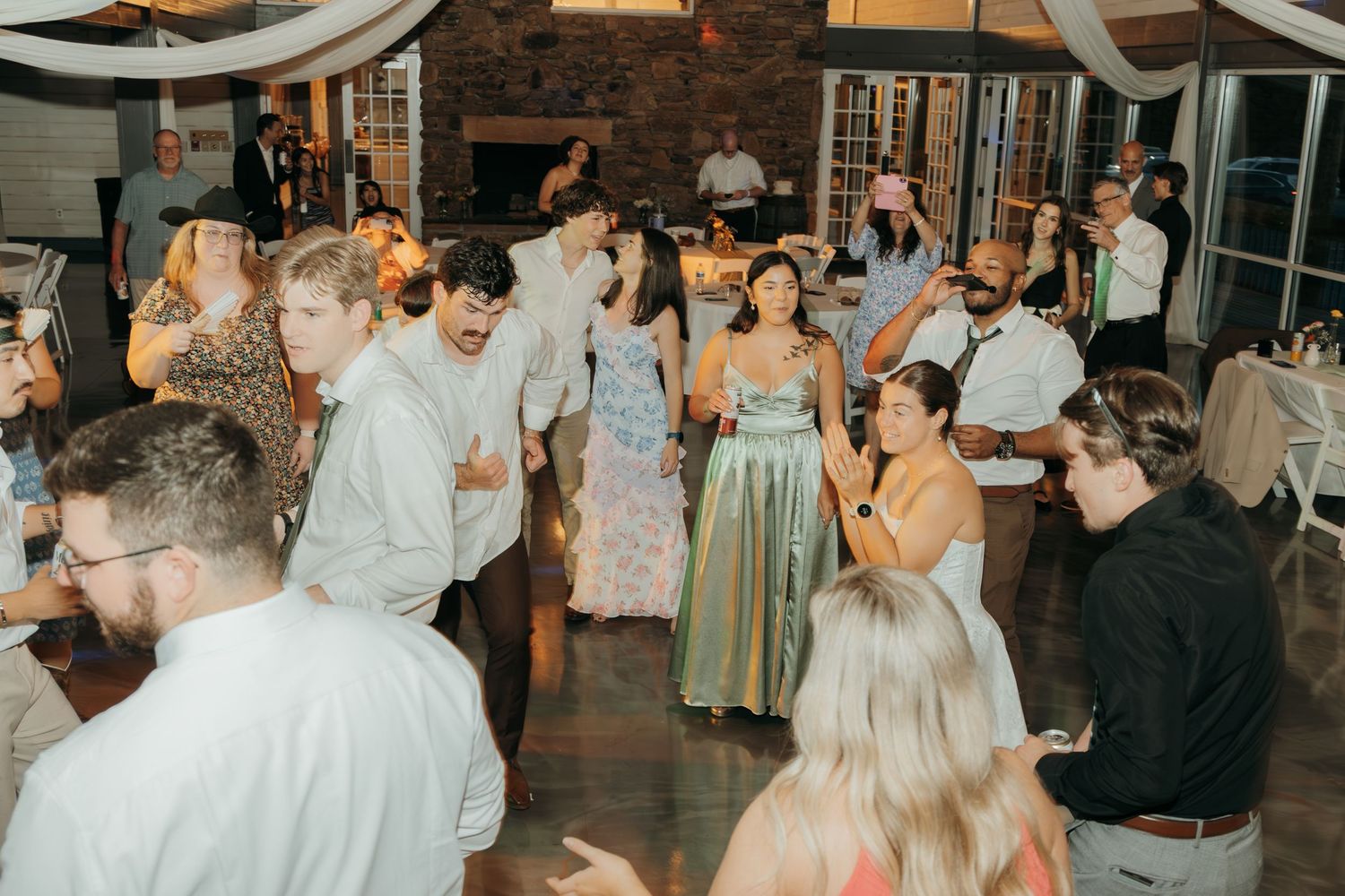 Wedding guests dancing together under elegant white fabric ceiling decorations at indoor reception.