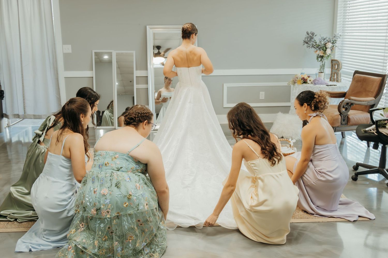 Bridesmaids help adjust wedding dress train during getting ready moments.