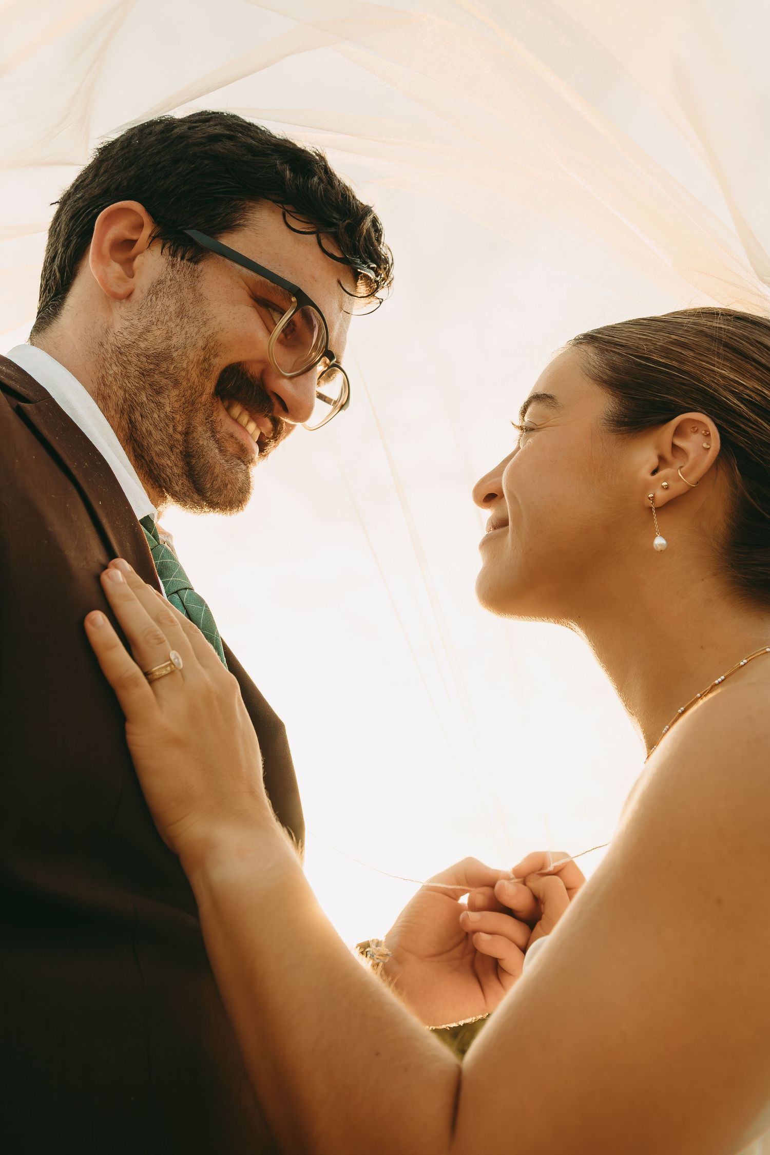 Close-up silhouettes of a bride and groom sharing an intimate moment against a bright backlit sunset.