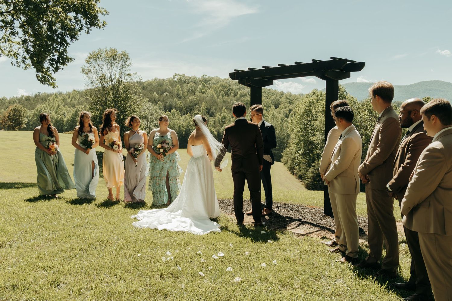 Wedding ceremony setup with guests seated on white chairs facing wooden arbor in mountain setting.