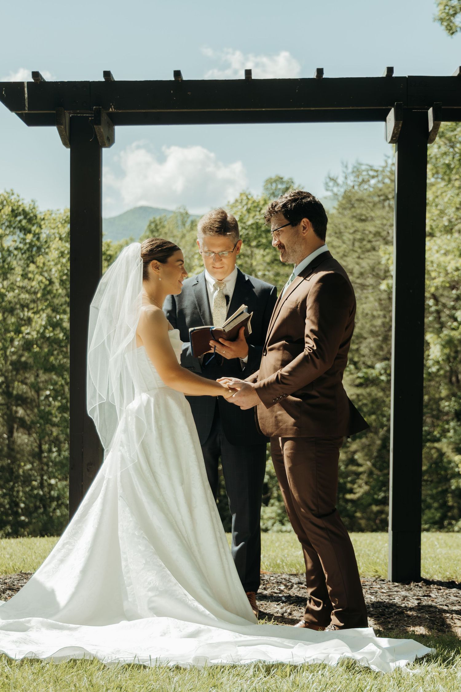 Couple exchanges vows under wooden pergola during mountain wedding ceremony.