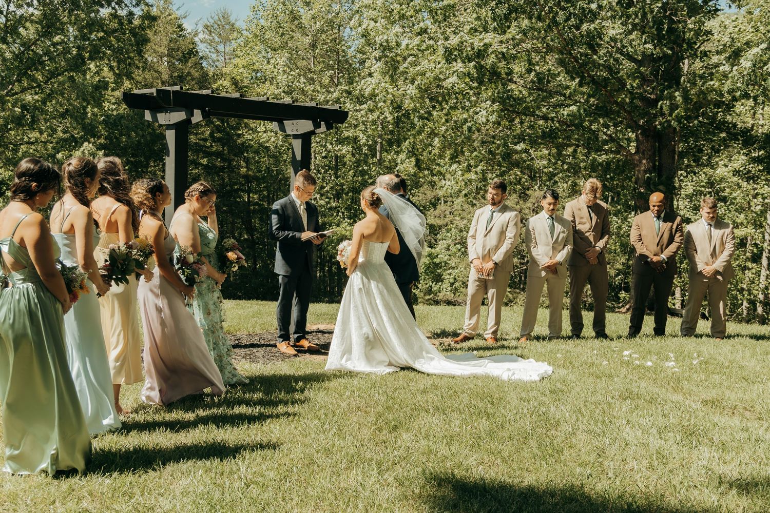Outdoor wedding ceremony under wooden pergola with mountain backdrop and bridal party.