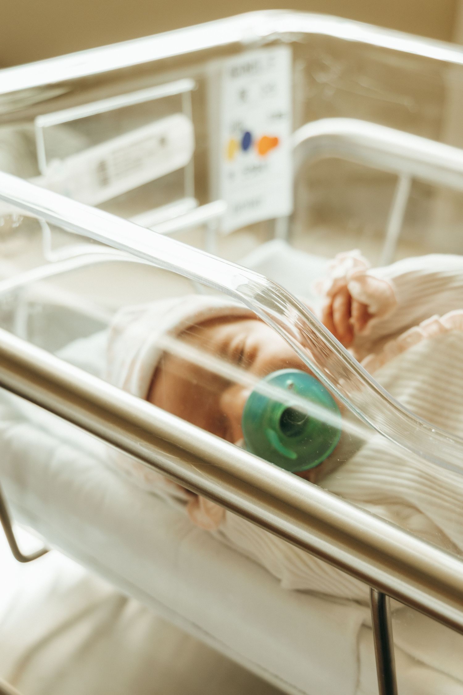Close-up of hands holding a medical device near a newborn incubator in a neonatal intensive care unit.