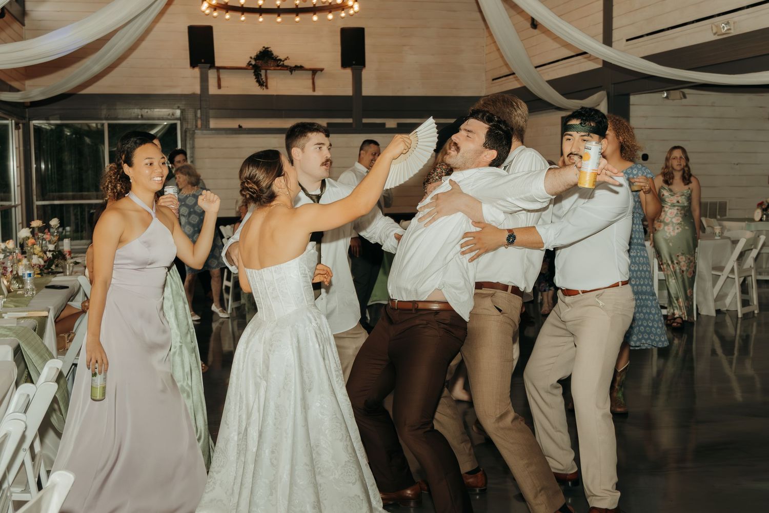 Lively wedding party dancing in coordinated gray and white outfits under elegant venue lighting.