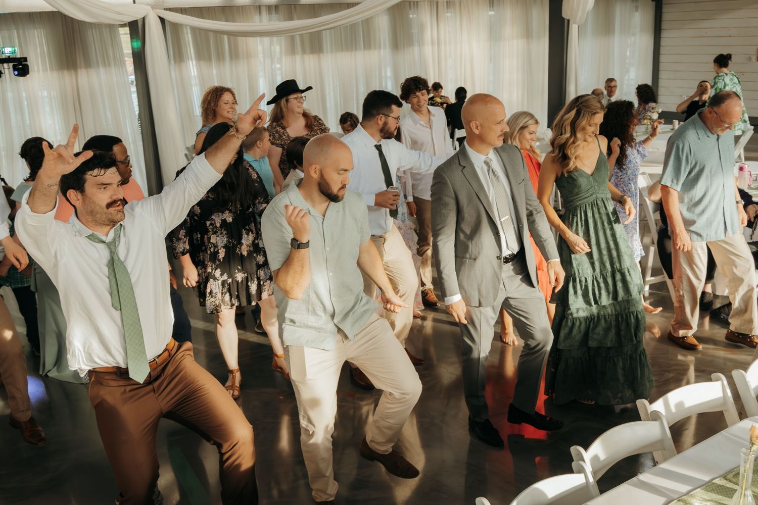 Panoramic view of wedding guests dancing and celebrating at an indoor reception venue.