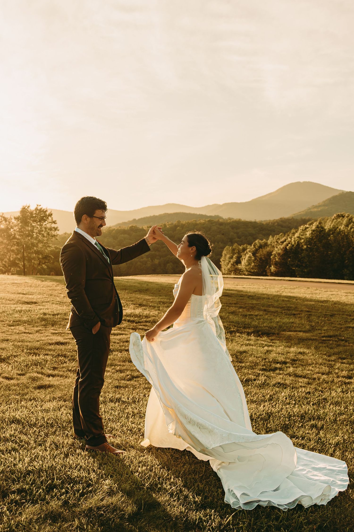 A couple shares a dance in a mountain field during sunset as the bride's dress flows in the wind.