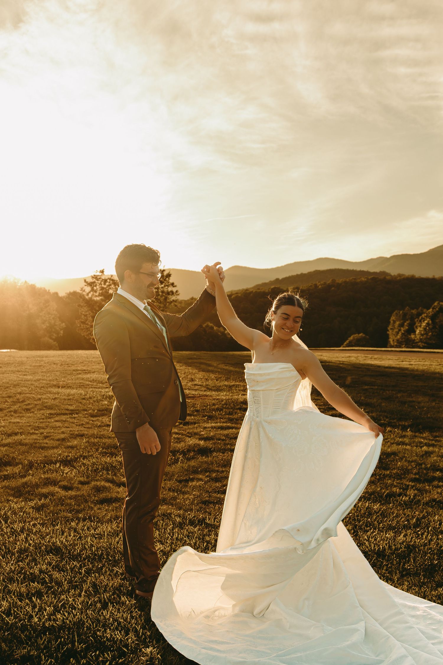 A couple dances in a field during golden hour as the bride's dress twirls beautifully.