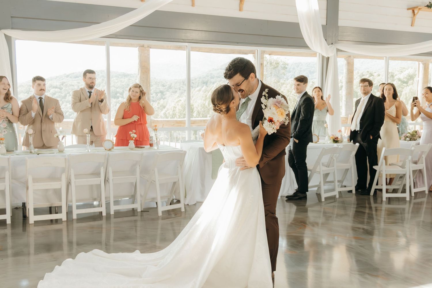 Newlyweds share their first dance at reception while guests watch from white chairs.