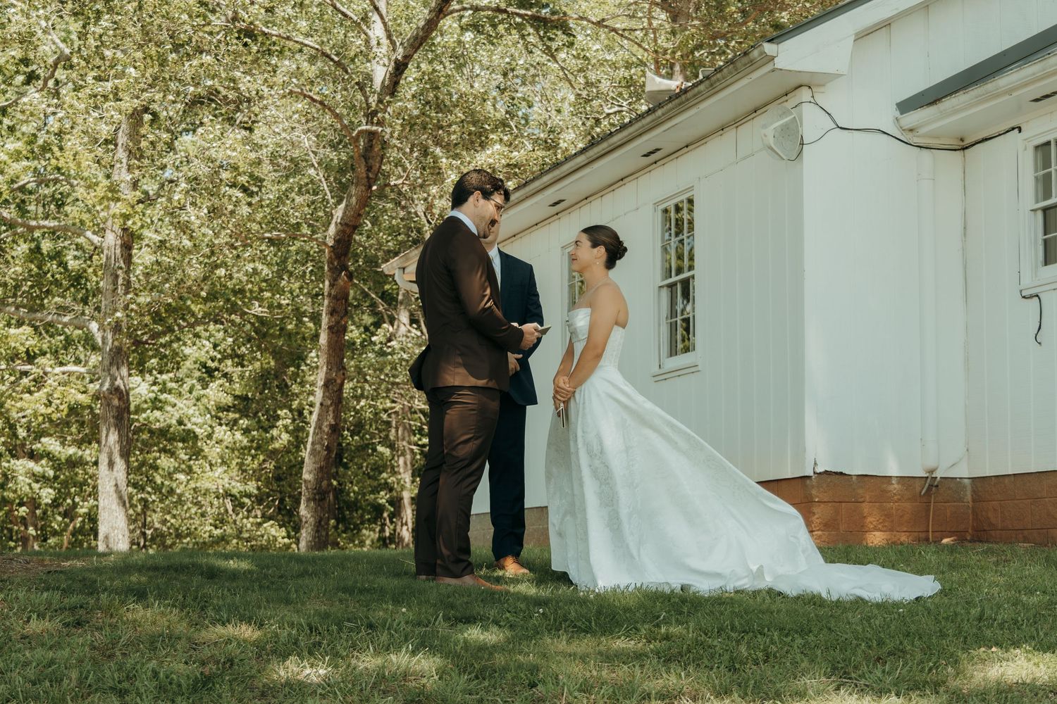 Wedding couple poses together against white chapel backdrop in natural lighting.