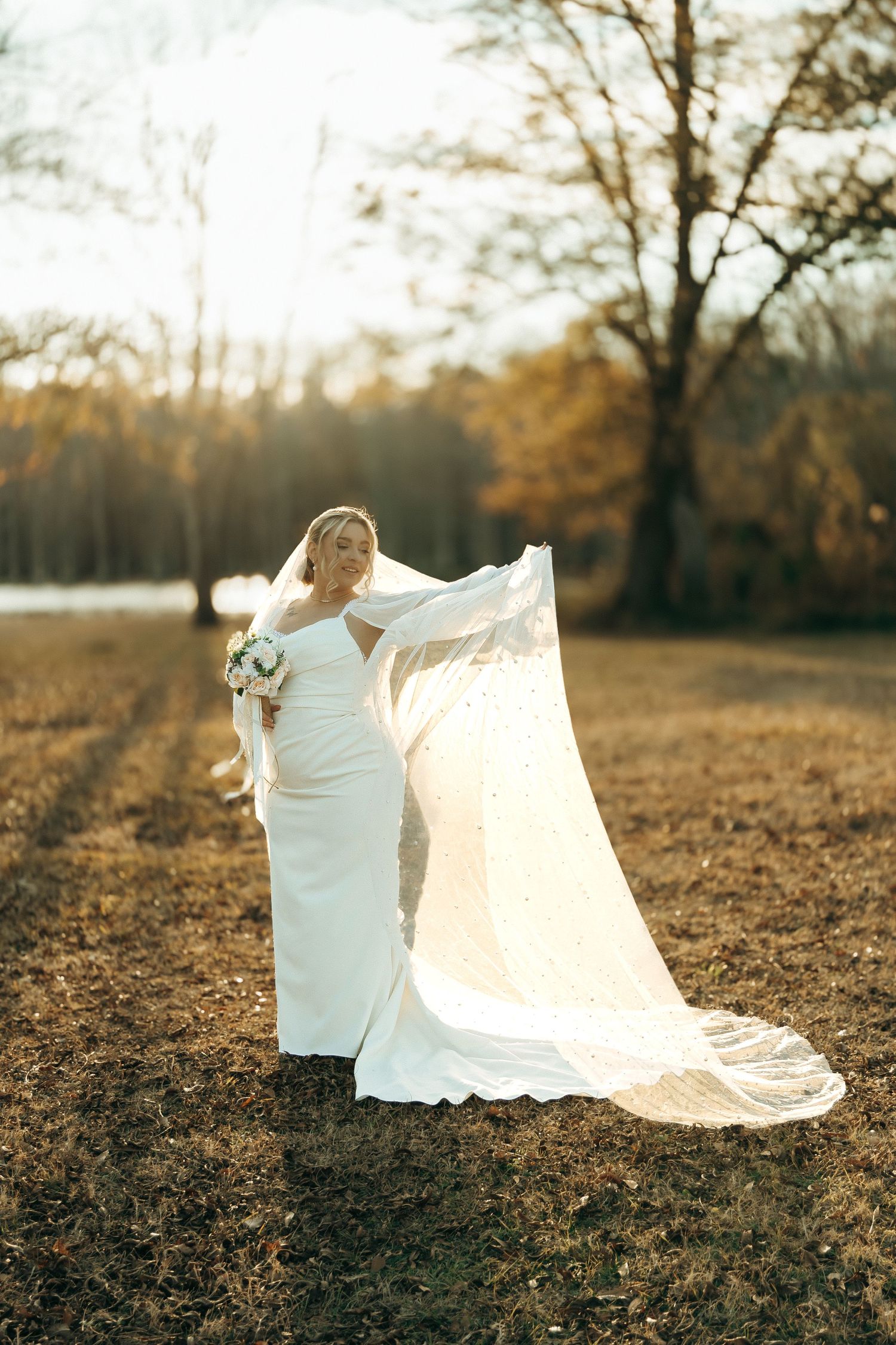 Ethereal bridal portrait with flowing veil backlit by golden sunset in autumn field.