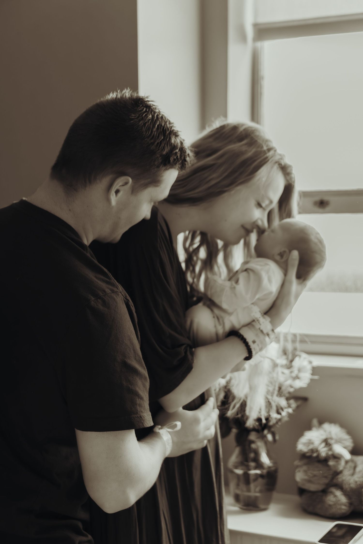 Black and white photo series showing couple in tender moment with soft window lighting and floral decor.