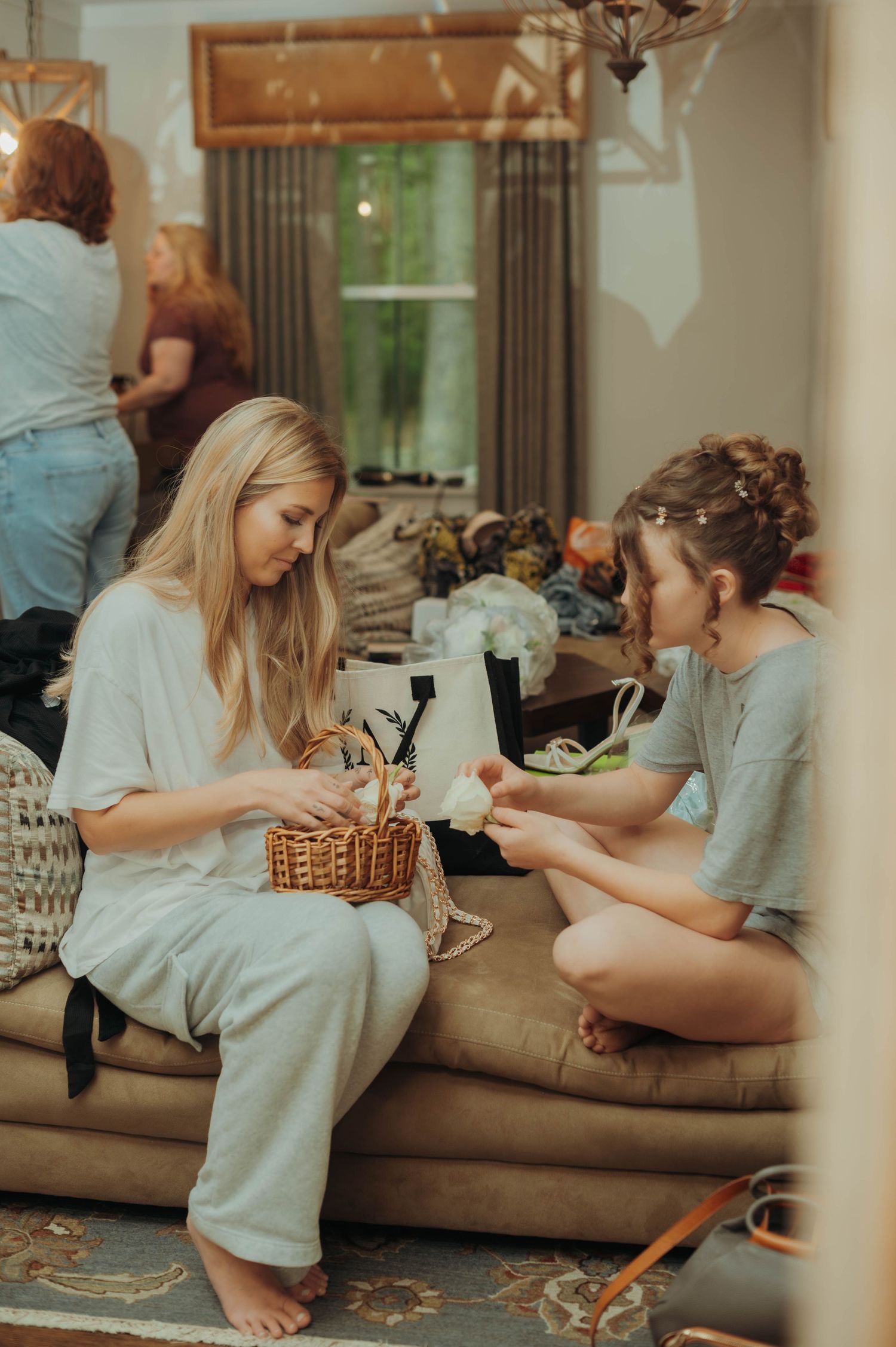 Two friends sitting on a couch sharing snacks from a wicker basket in a cozy living room setting.