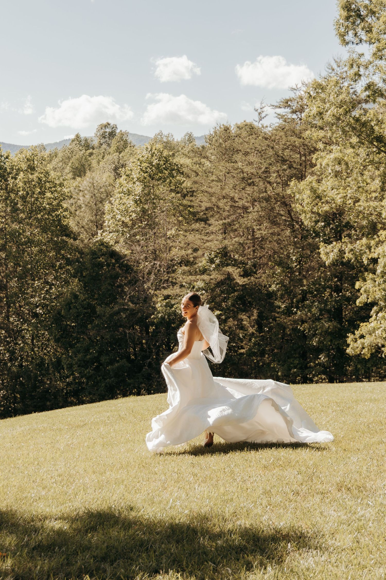 Bride spins in her flowing wedding dress on a hilltop with forest backdrop.