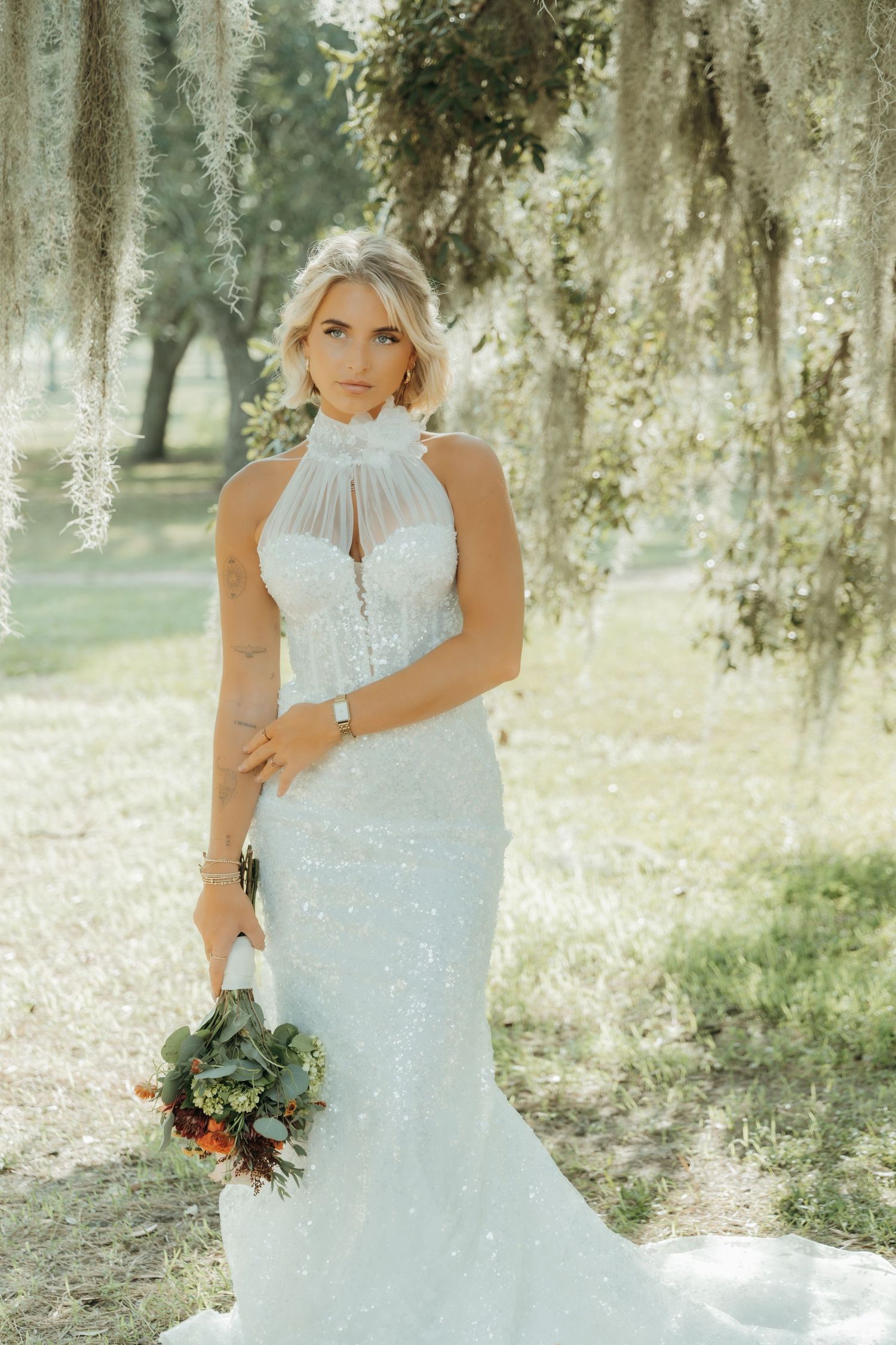 A bride in a white lace wedding dress poses under Spanish moss in a dreamy outdoor setting.