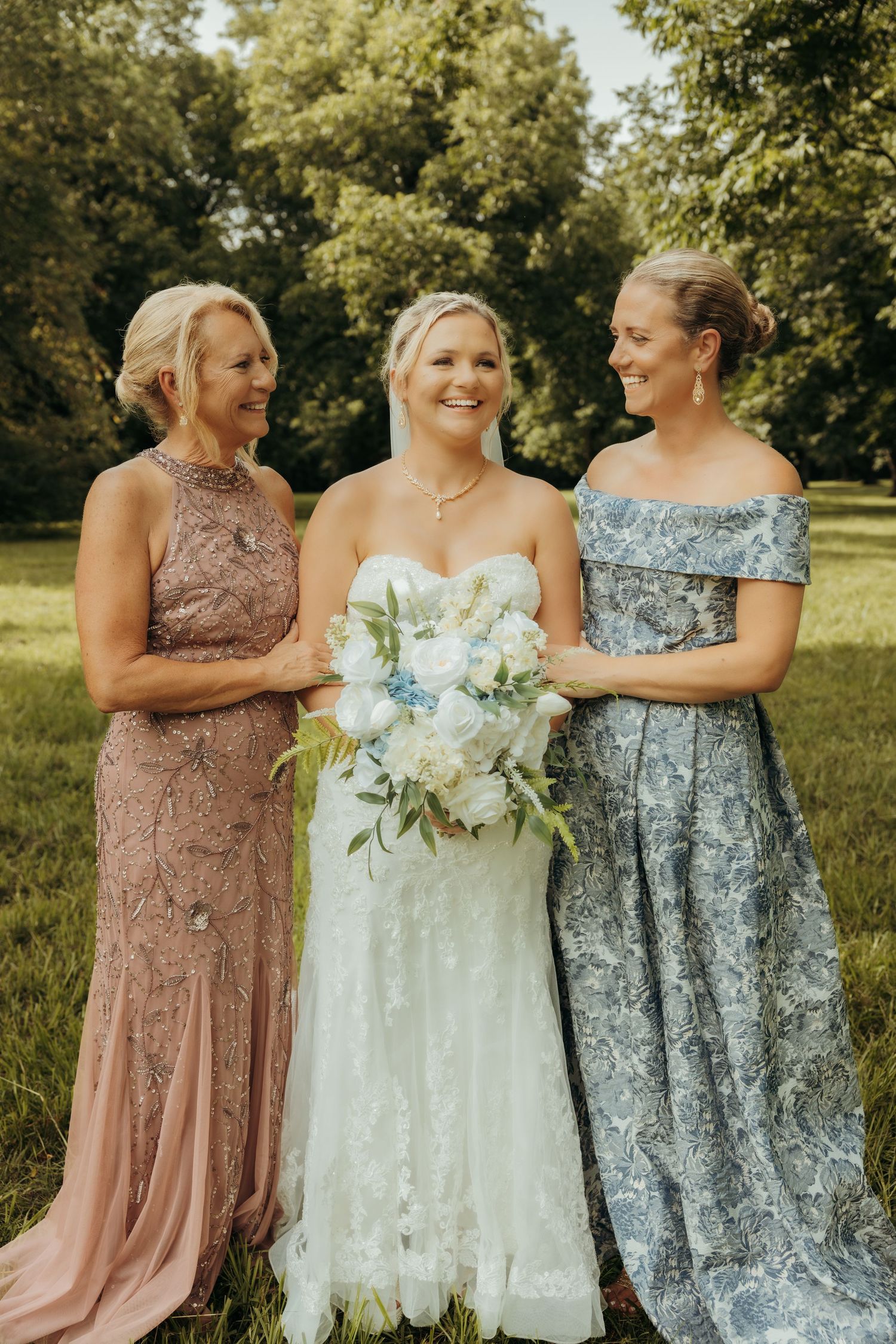 Wedding party members in dusty rose and silver dresses share candid moments outdoors on a sunny day.