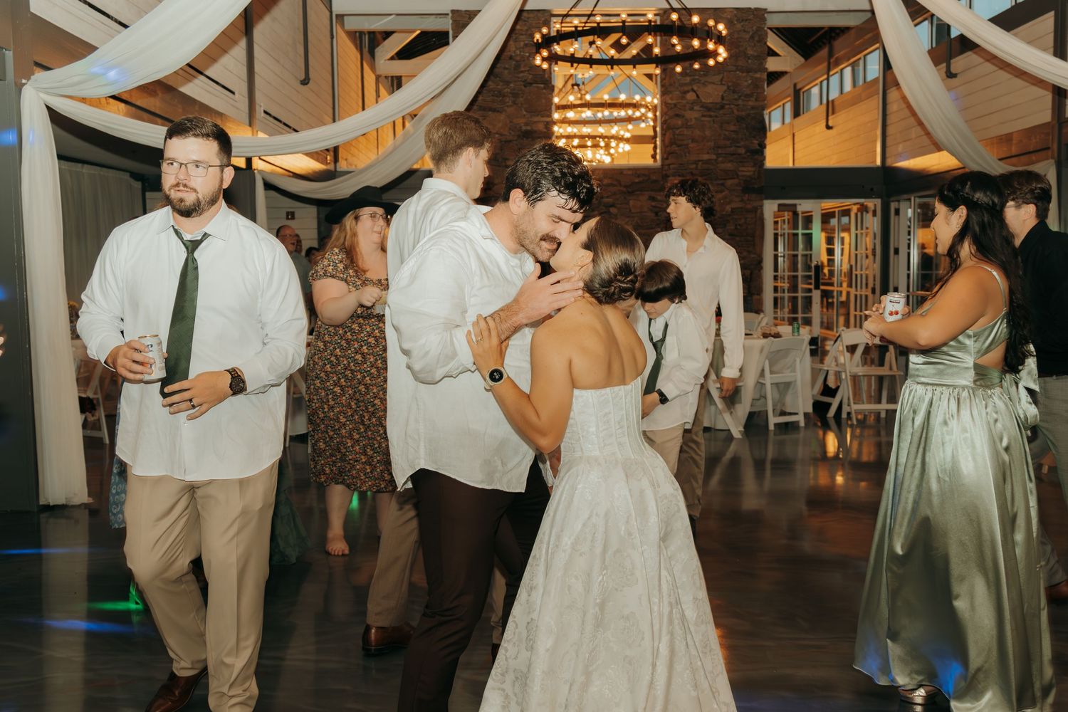 Wedding reception dance floor filled with guests in formal attire under elegant white ceiling drapes.
