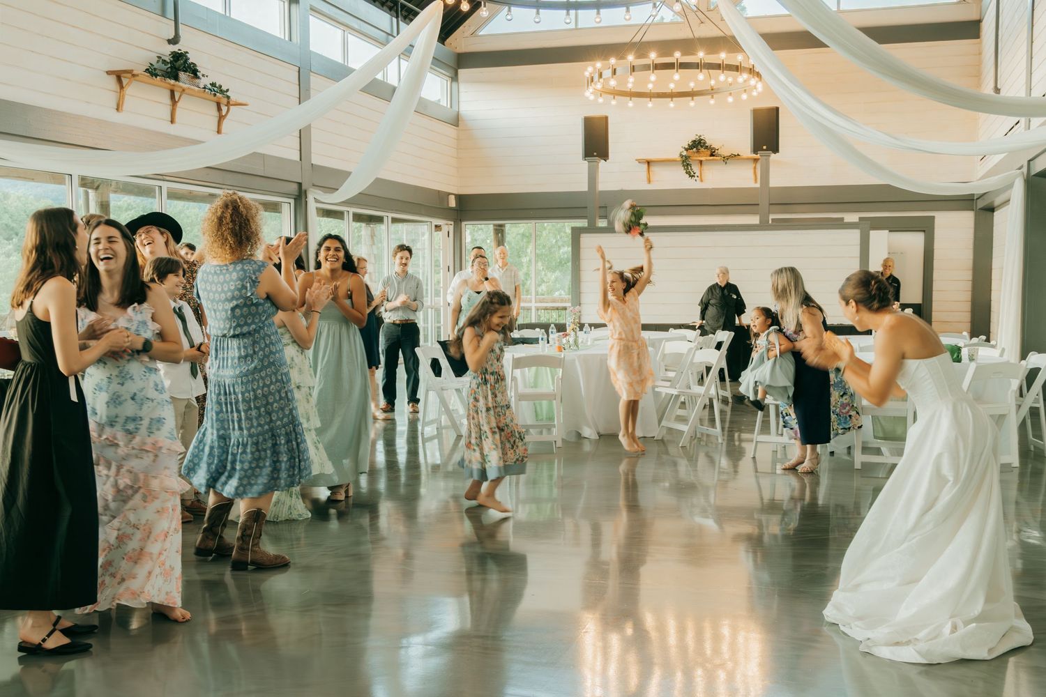 Festive wedding reception scene with guests dancing under white ceiling drapes.