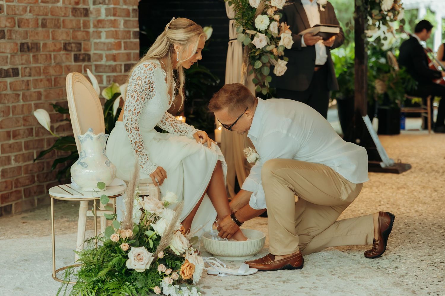 A traditional foot washing ceremony takes place during a wedding with white floral decorations.
