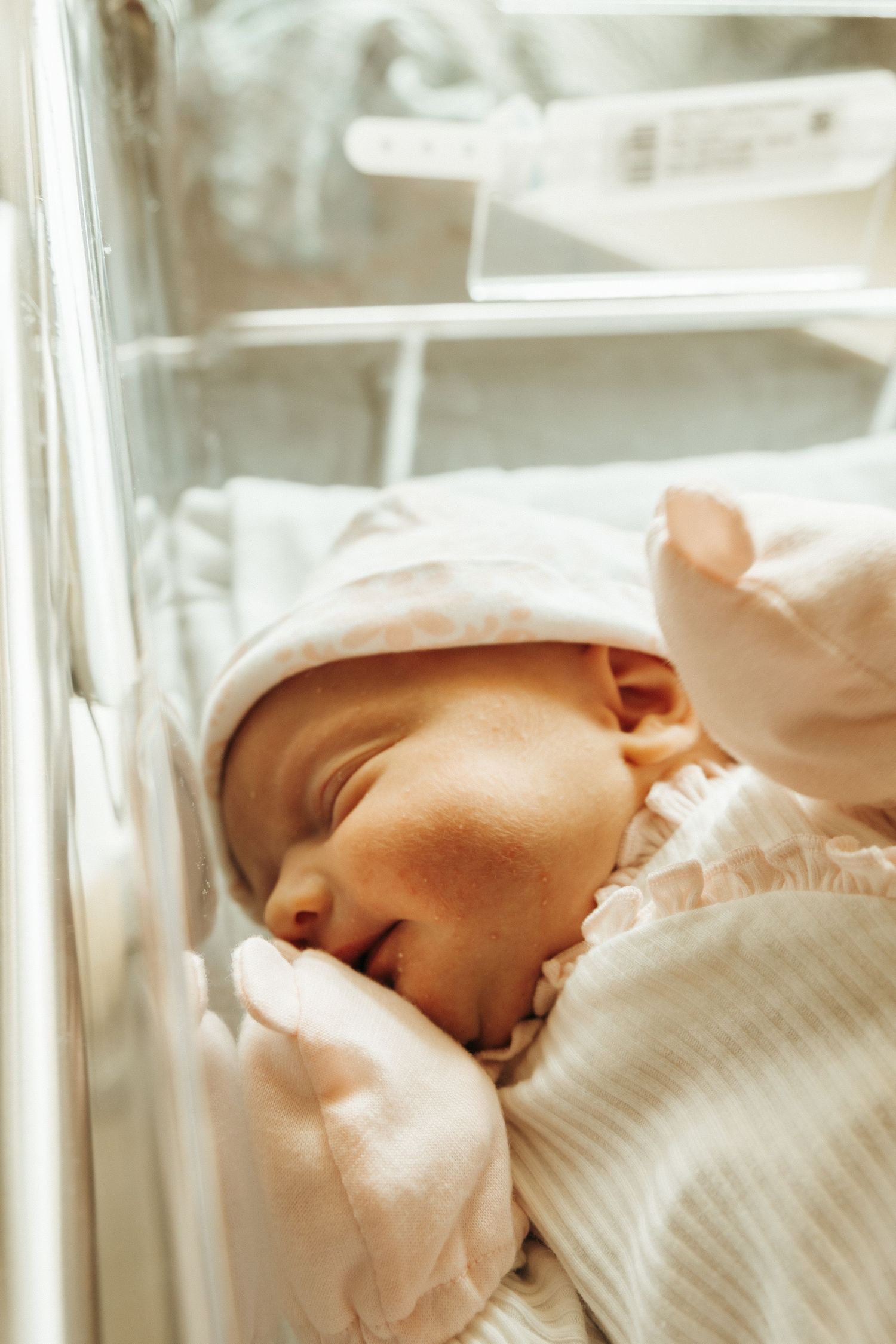 Newborn baby sleeping peacefully in a white hospital bassinet under soft lighting.