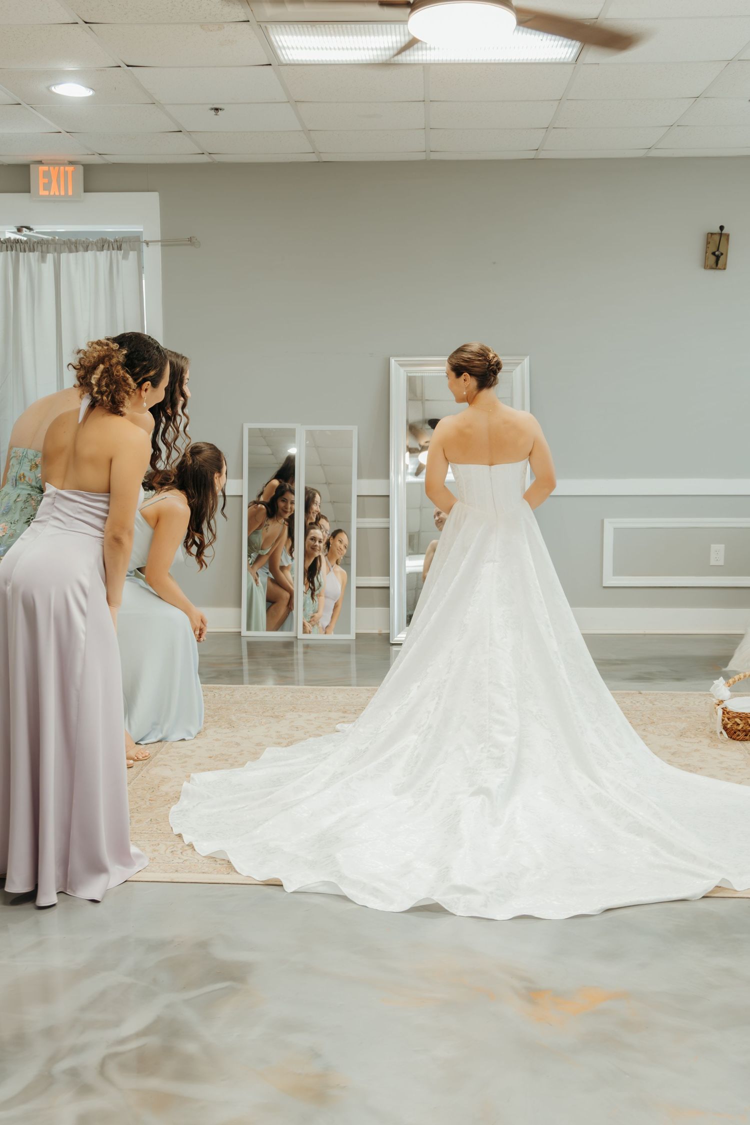Bride tries on wedding dress while bridesmaids admire the long train in dressing room.