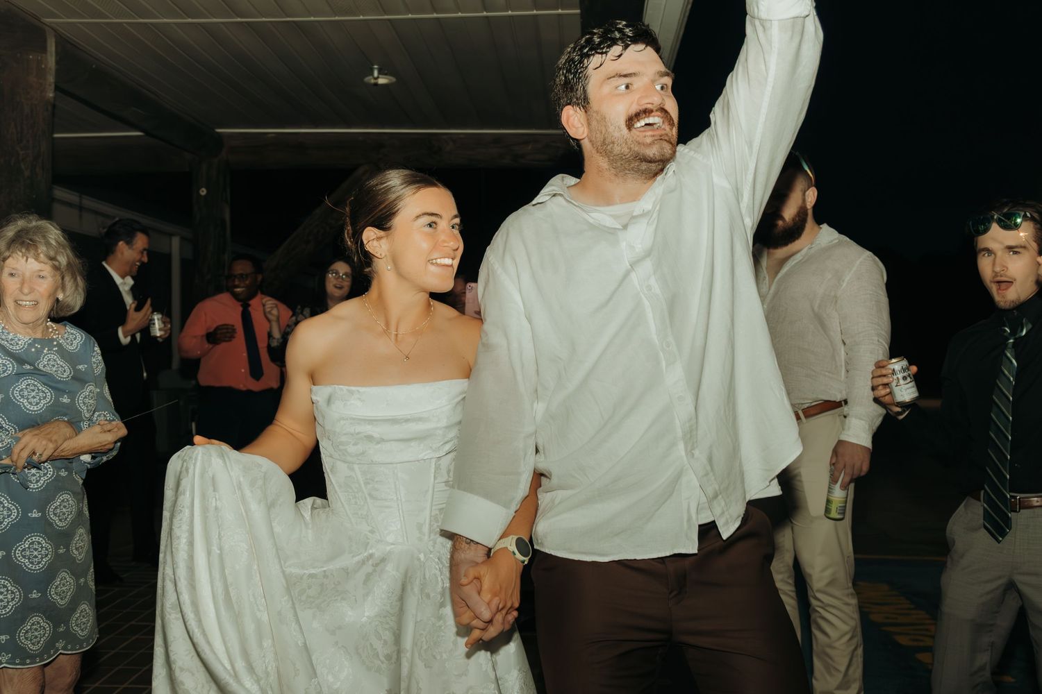 Wedding celebration with guests dancing and raising hands on dimly lit dance floor.